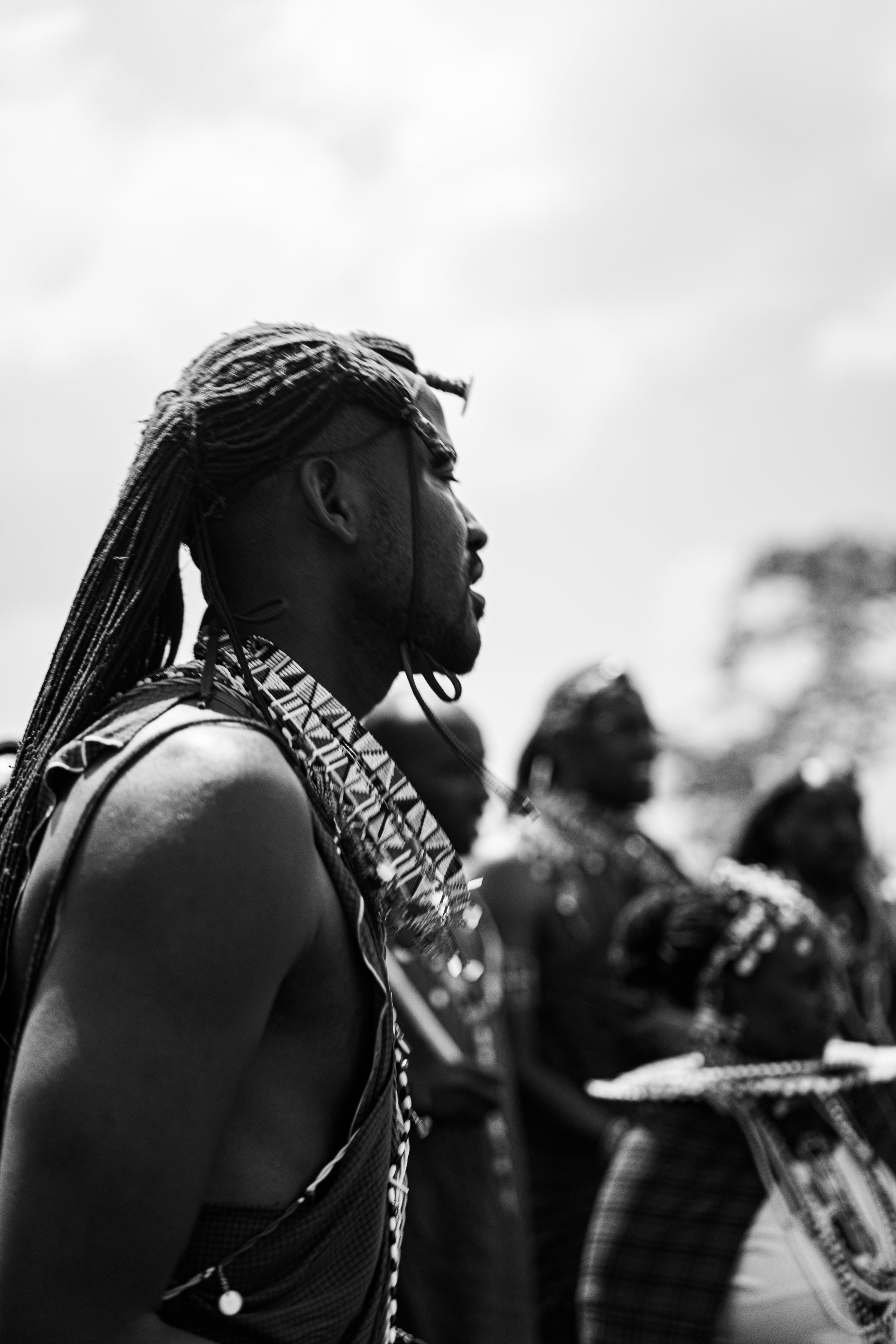 A black and white photo of a woman with long, braided hair looking to the side during an outdoor event.