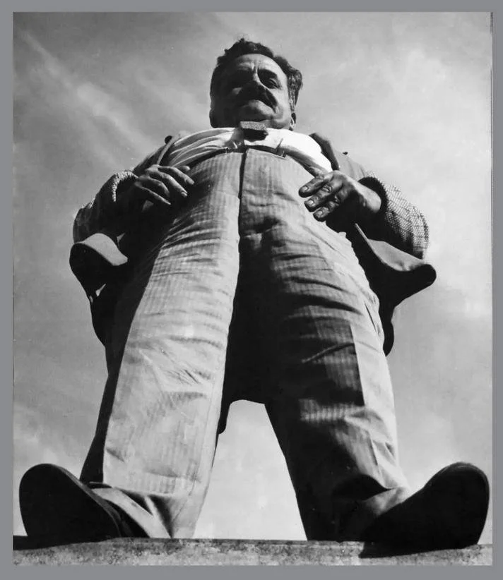 Black and white archive photograph of a man standing outdoors.