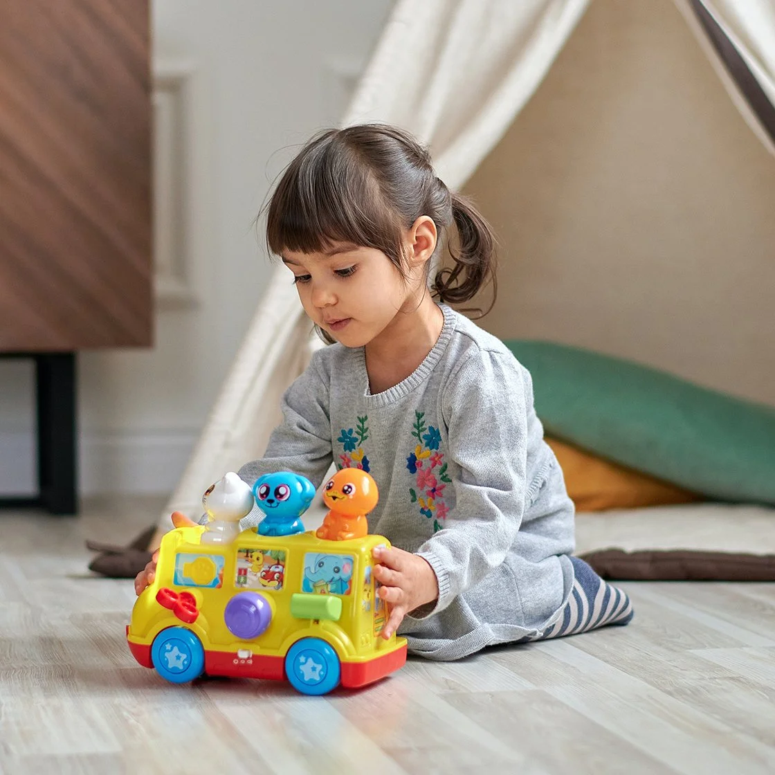 A young girl playing with a colorful toy bus on the floor.