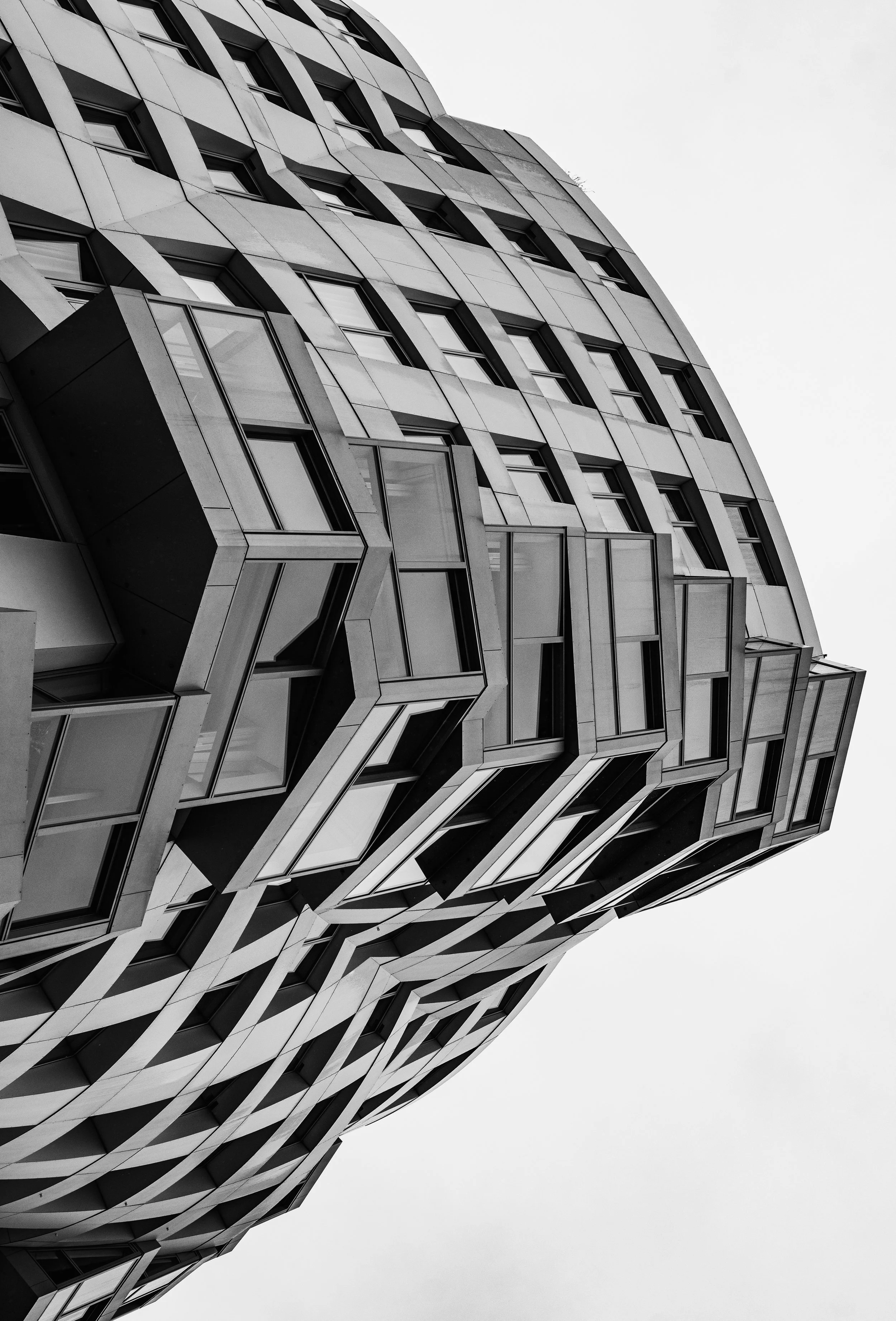 A modern, geometric building with an intricate design of windows and panels, shown from a low angle against a cloudy sky.