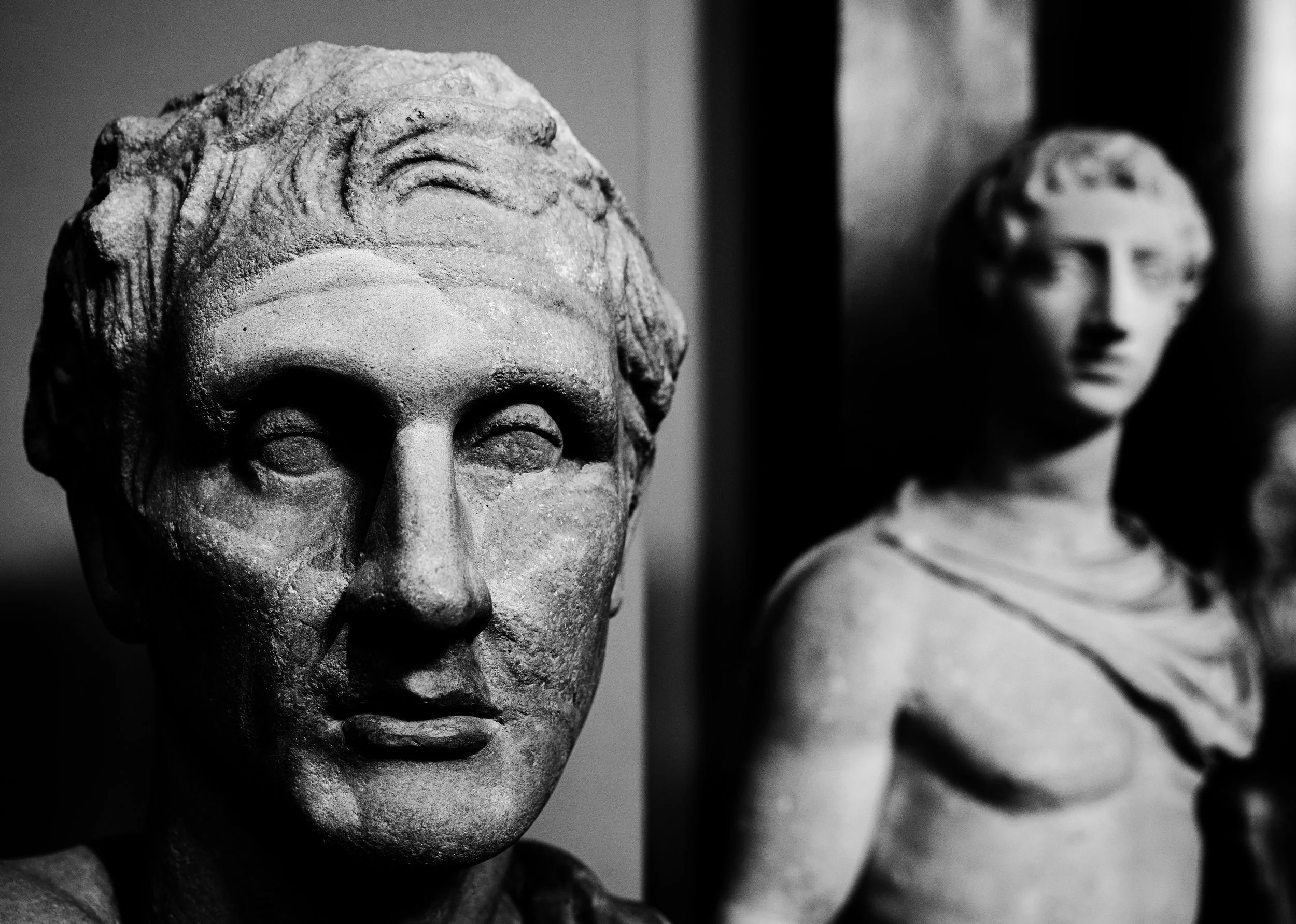 Black and white photo of ancient stone sculptures, with a close-up of a male bust with carved hair on the left and a partially visible female bust on the right.