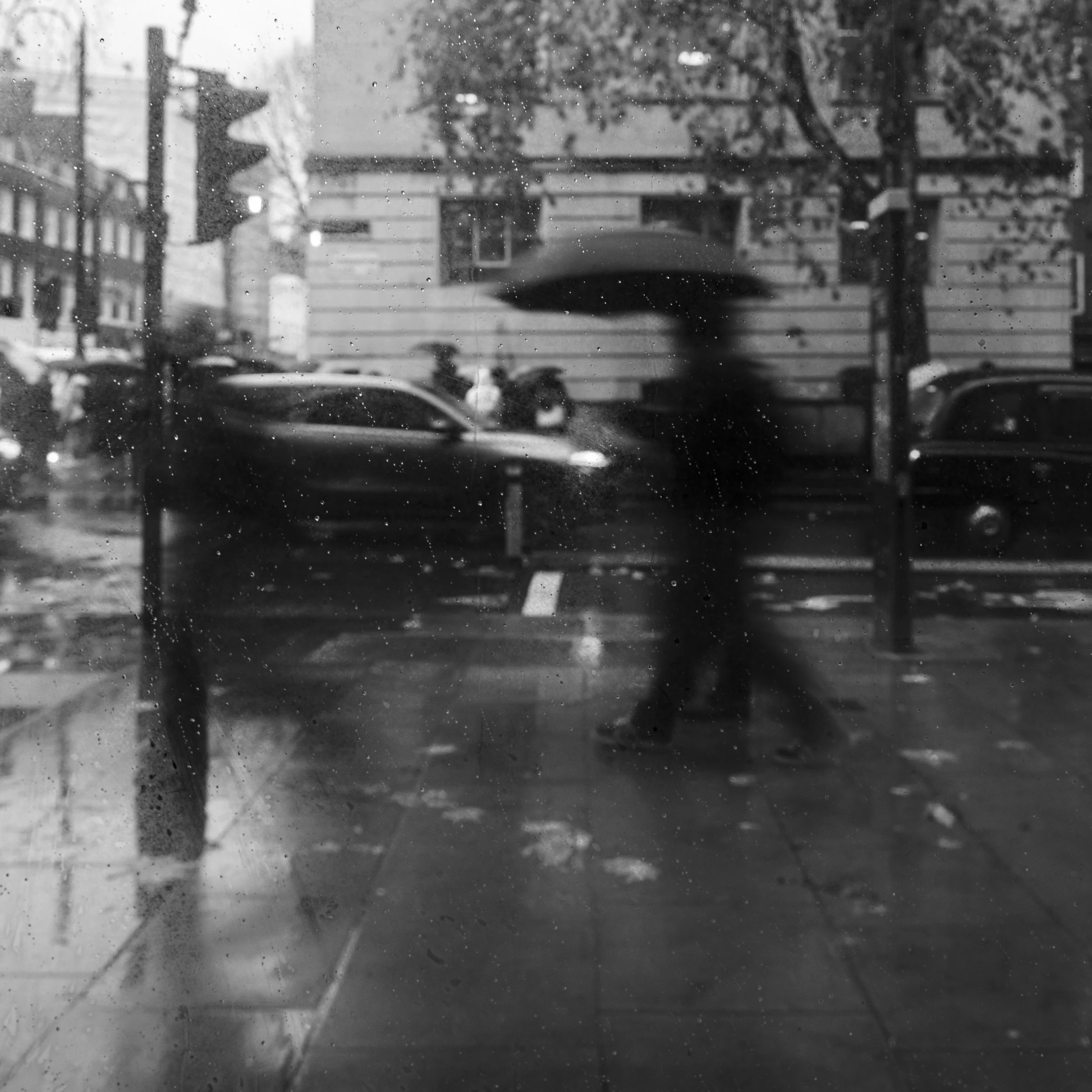 A person walking with an umbrella on a rainy day in an urban setting, view through a wet glass window.