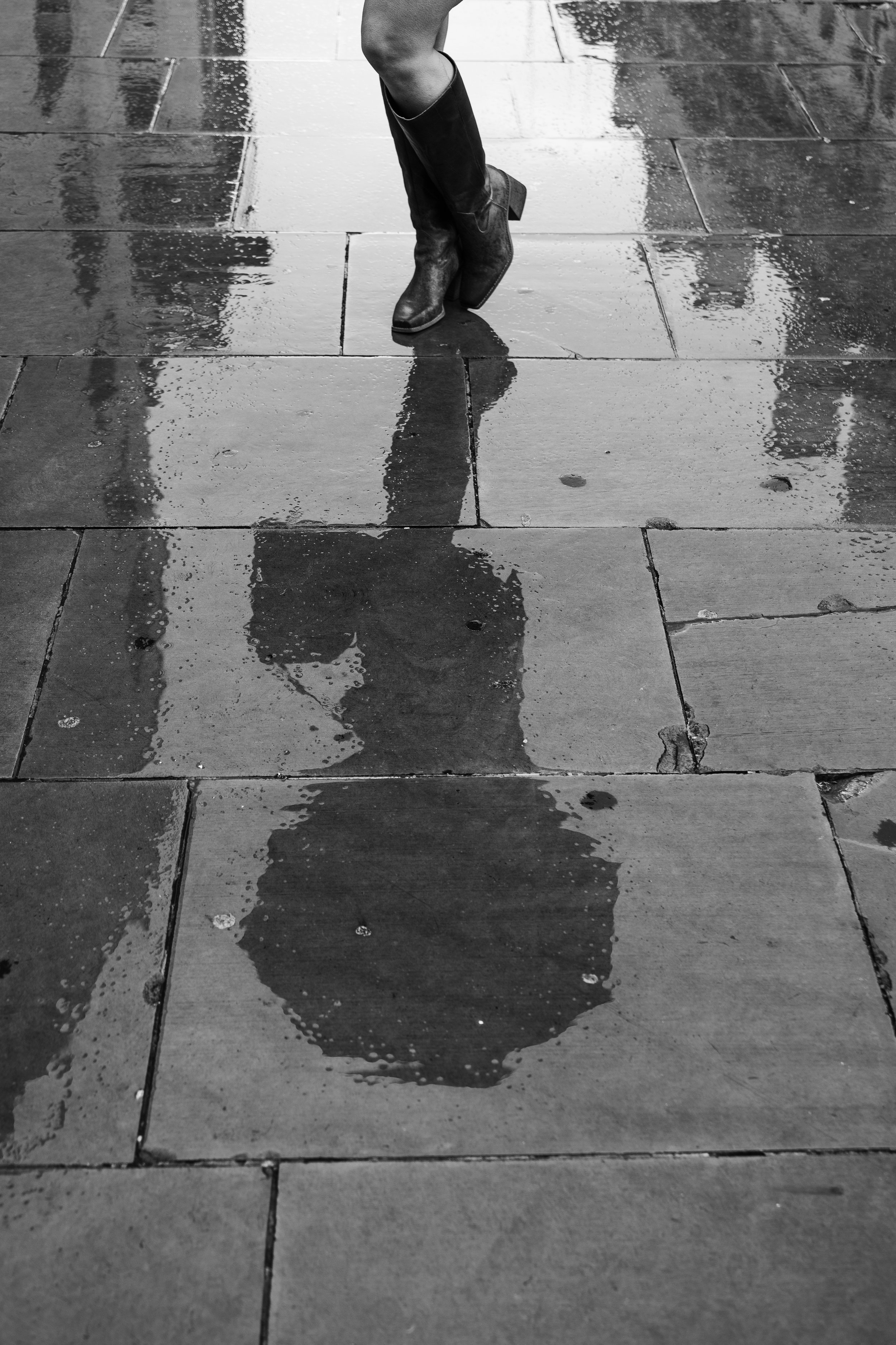 Reflection of person wearing heels on wet sidewalk tiles.