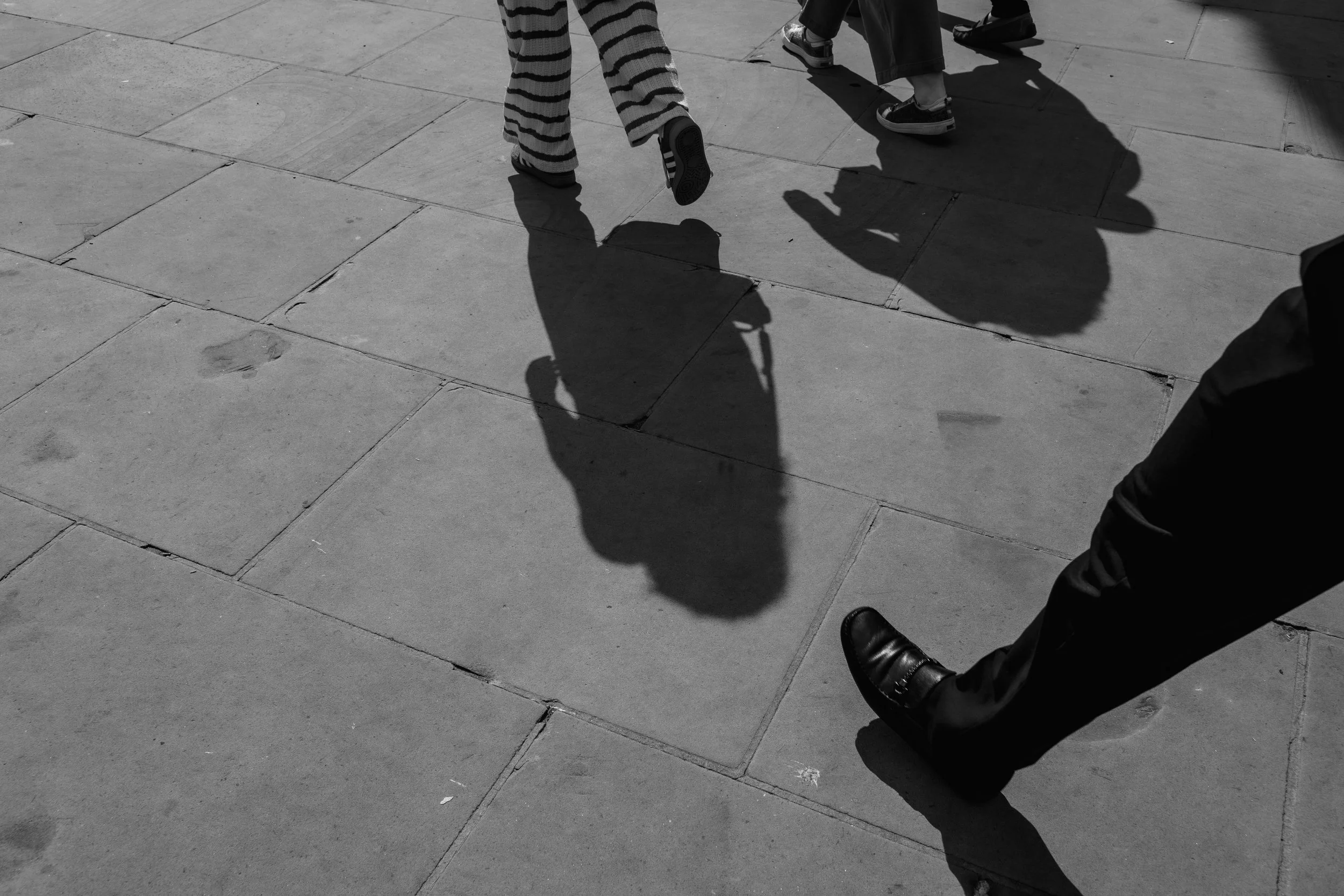 Shadow of a man walking on a sidewalk with other people, captured from below.
