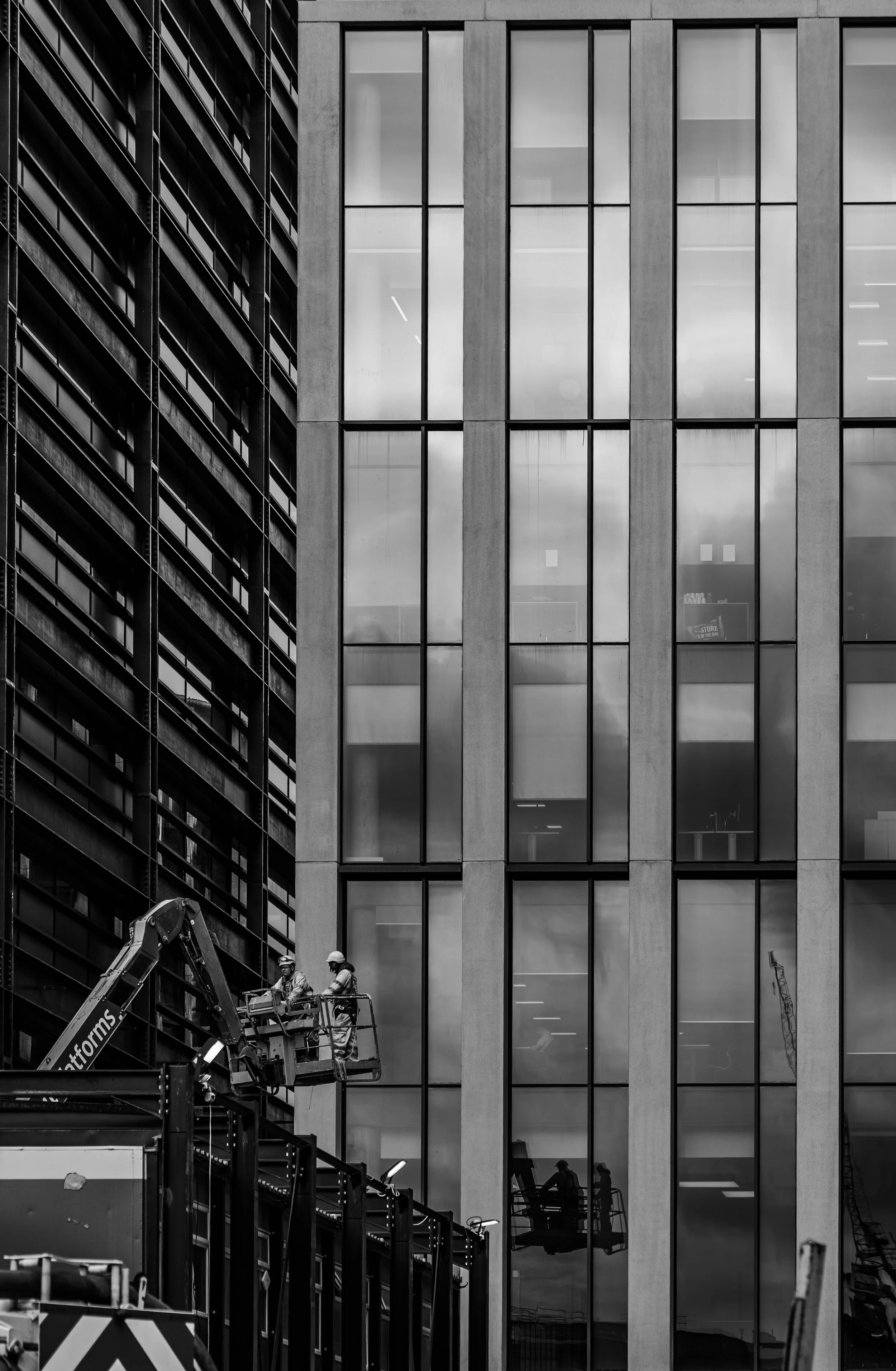 Black and white photo of construction workers on a lift working in front of a modern office building with large glass windows.