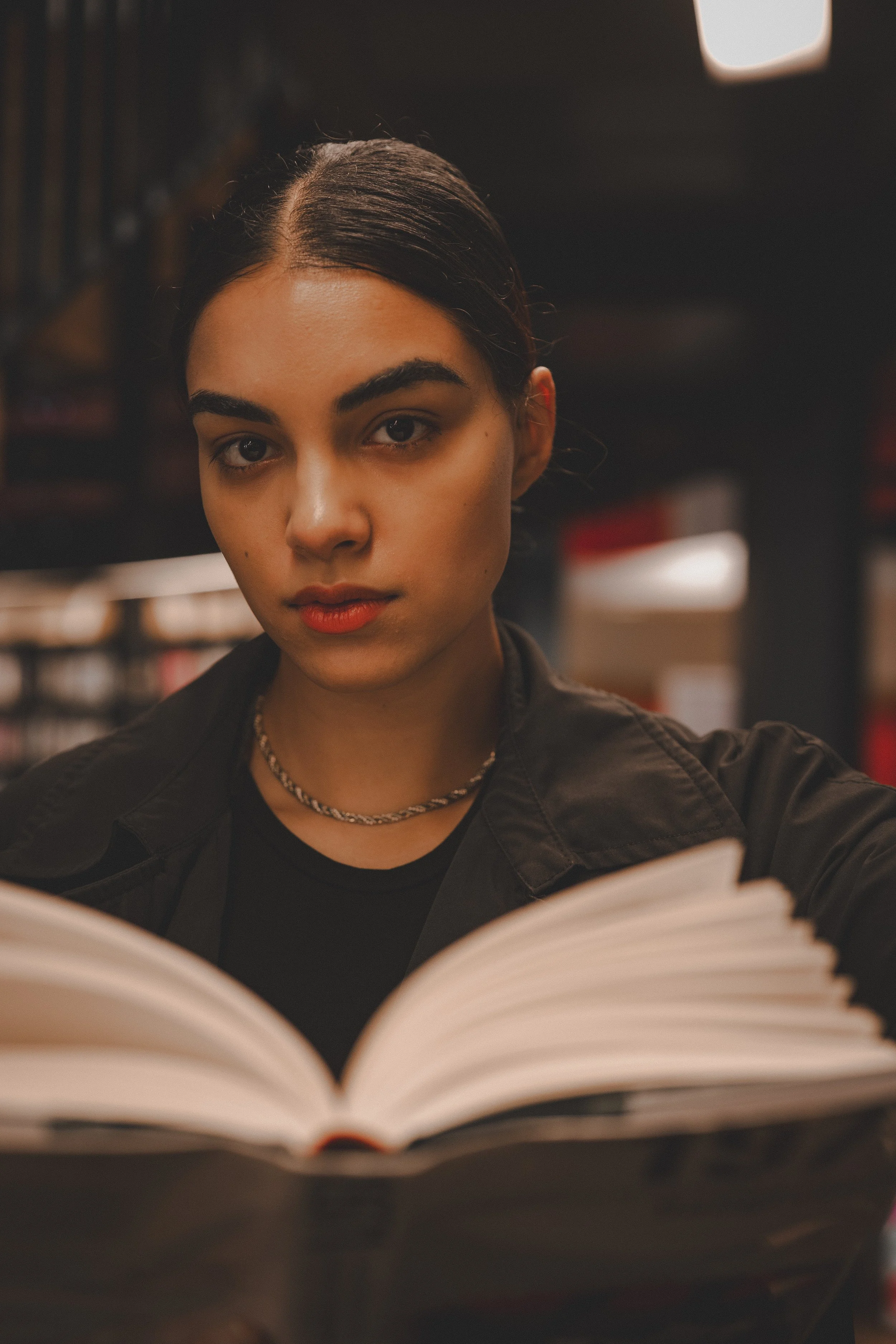 A cinematic portrait of a young woman reading a book in a library, conveying concentration, knowledge, and a love for literature.