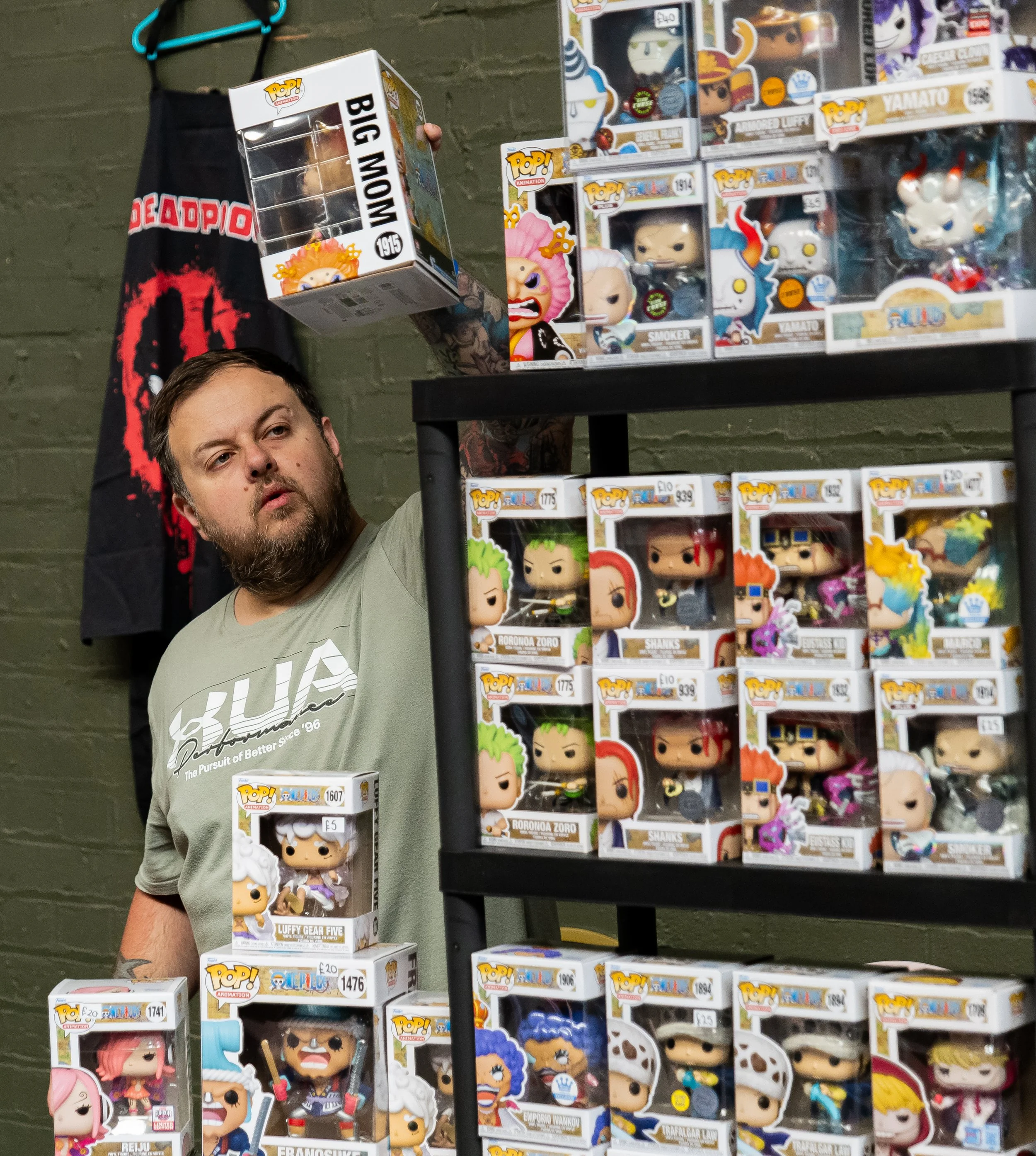 A man at a pop culture merchandise store, surrounded by boxed collectible figures from popular anime and gaming franchises, including Funko Pop! figures.