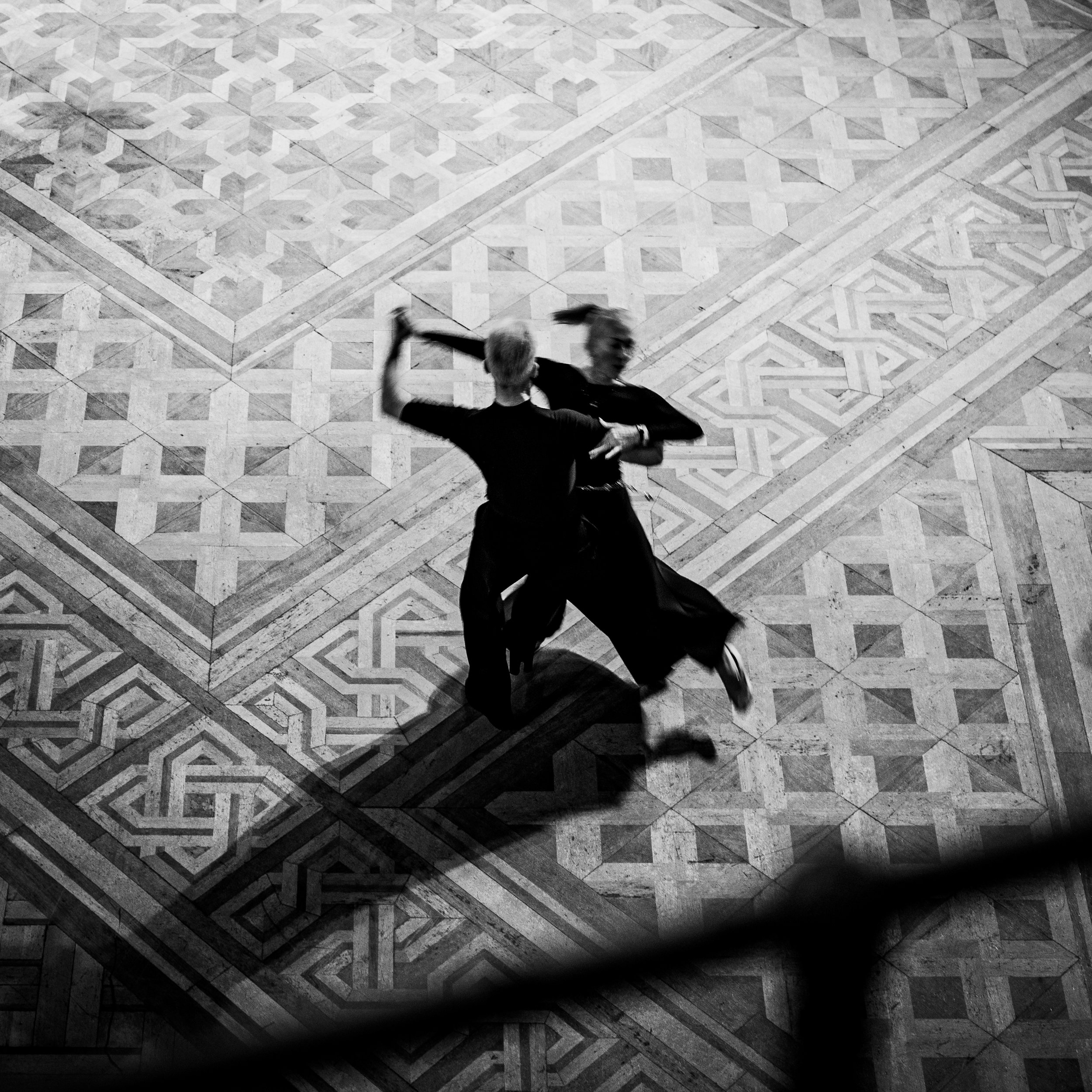 Two people dancing on a patterned floor, visible from above, in black and white.