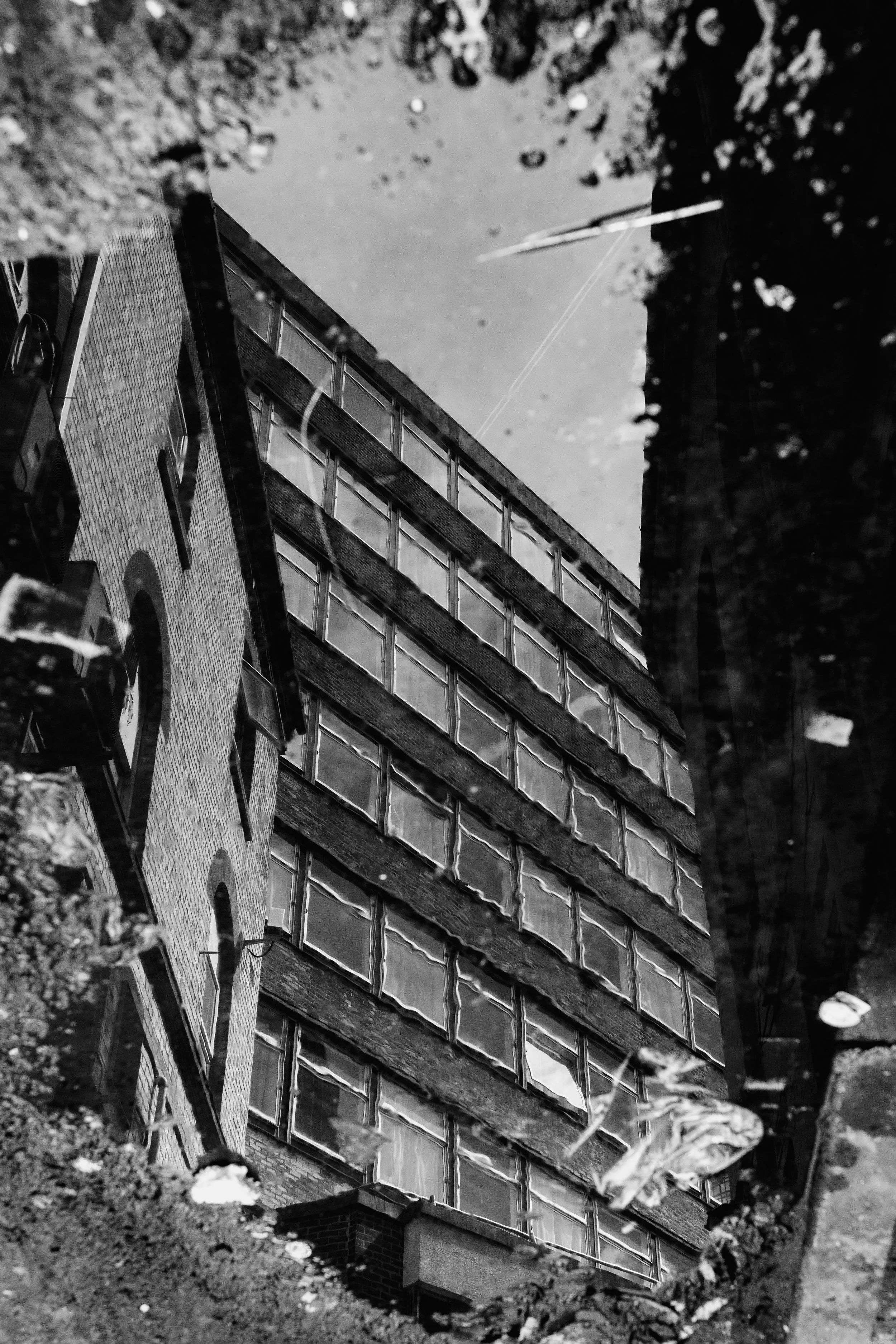 Reflection of an urban building with multiple windows in a puddle on the ground, black-and-white photo.
