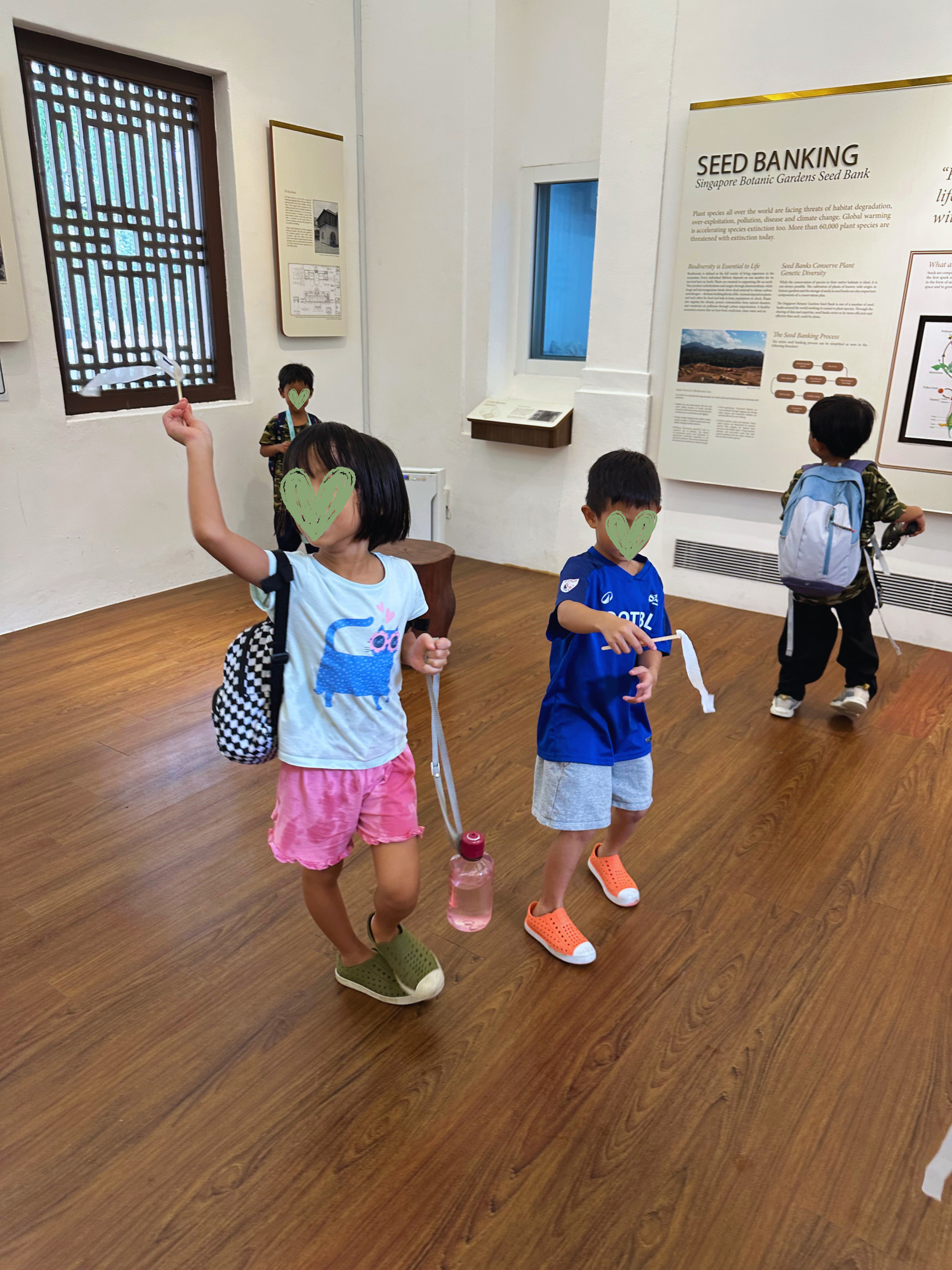 Four children walking in a museum, with informational posters on the wall and wooden flooring.