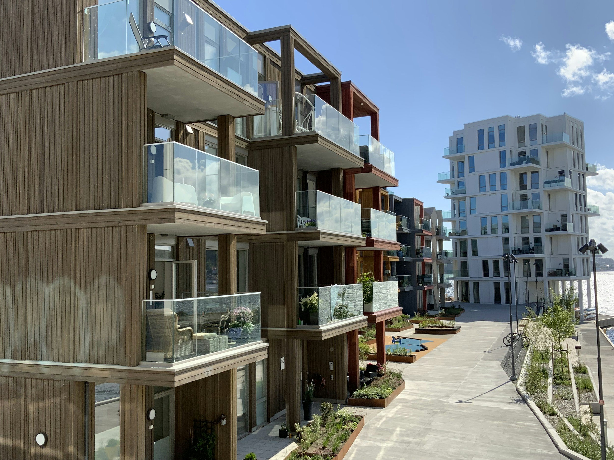 Modern apartment buildings with glass balconies along a paved walkway under a blue sky.