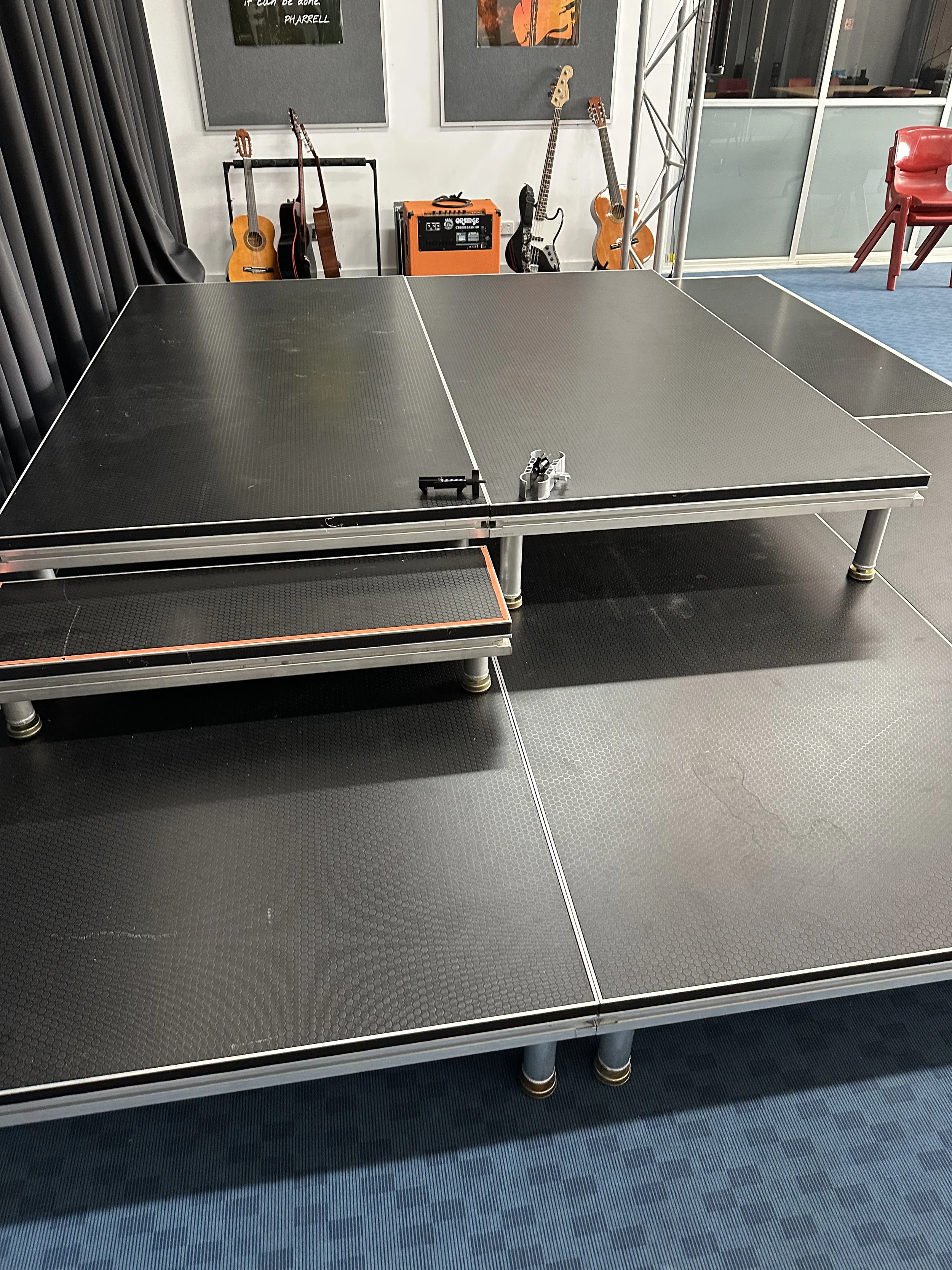 Indoor recreational room featuring a black ping pong table with paddles and ball, surrounded by musical instruments including guitars and an amplifier, with artwork on the wall and seating in the background.