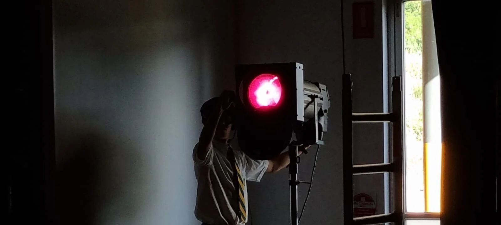 Person standing inside near a large red traffic signal with an illuminated 'don't walk' symbol, next to a window with sunlight coming through.