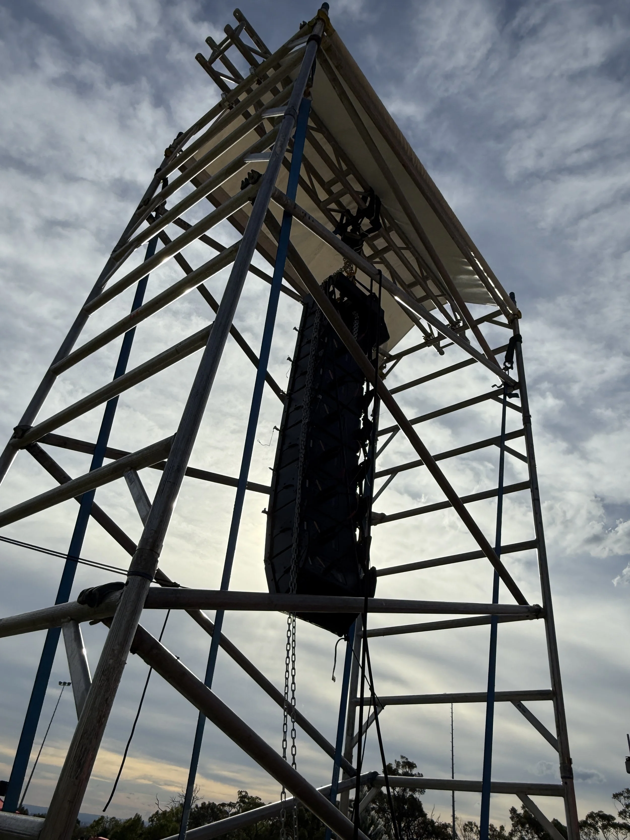 A tall scaffolding structure with a stage or platform at the top, set against a cloudy sky at sunset or sunrise.