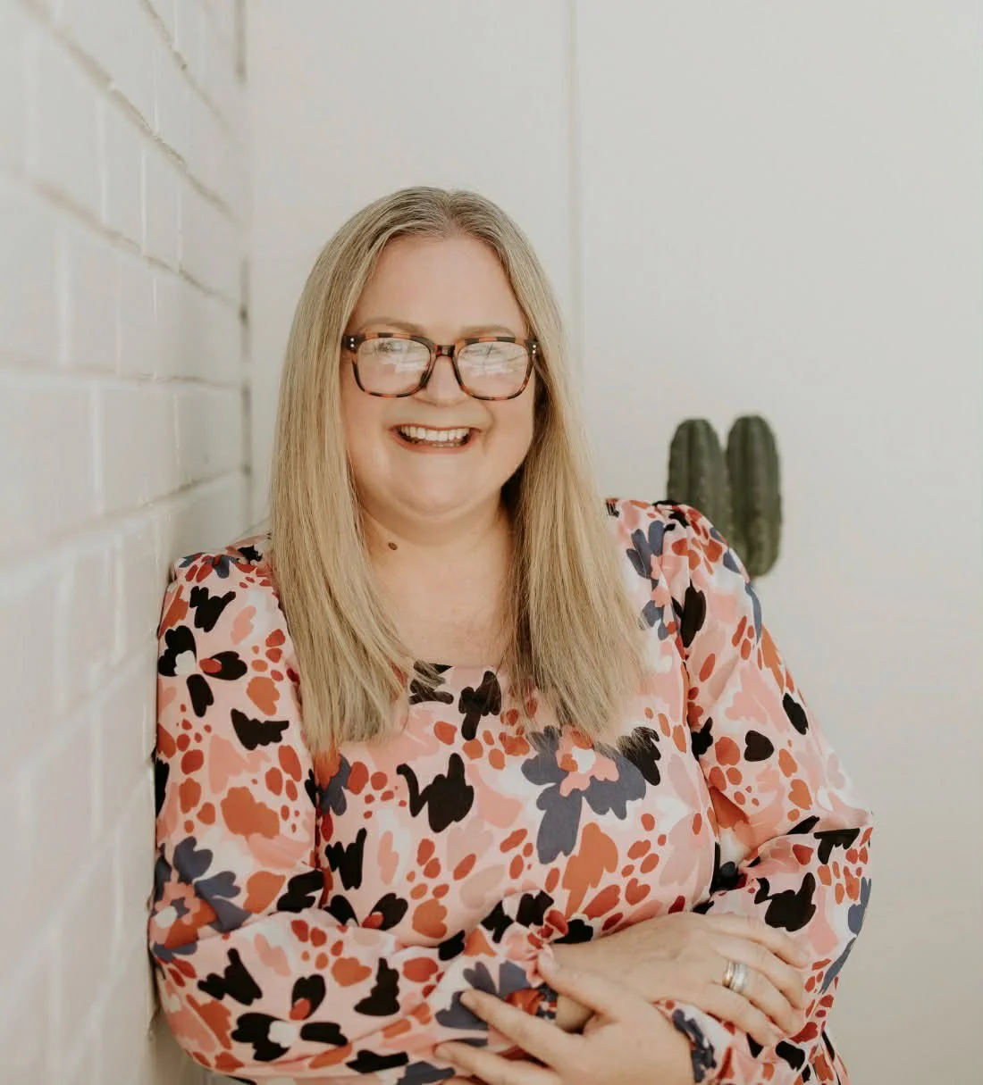 A woman smiling with glasses, hoop earrings, layered necklaces, and wearing a striped top.