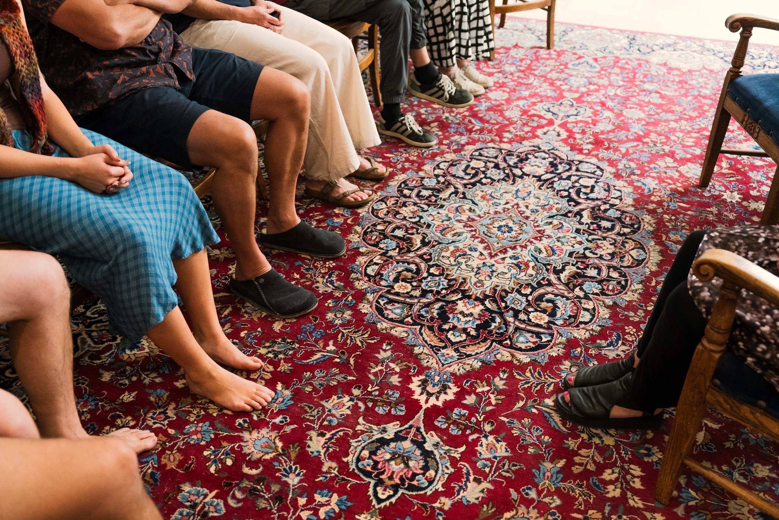 People sitting in a semi-circle in a room with a patterned red and blue rug. The Self Sanctuary