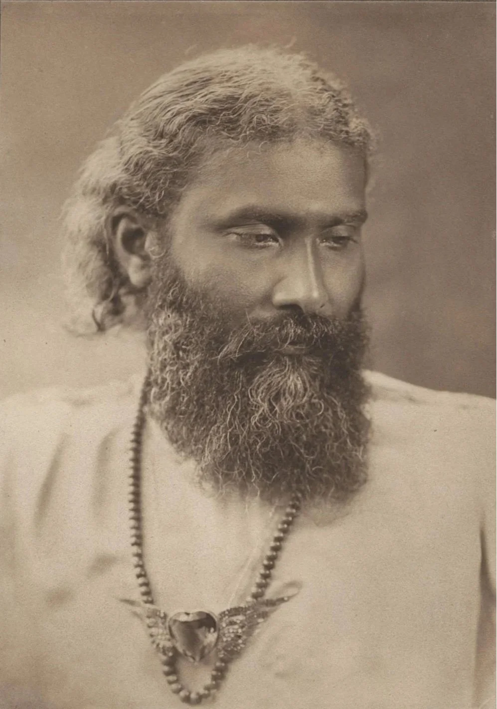 Sepia portret van Hazrat Inayat Khan, die een ketting met een hartvormige hanger draagt, oftewel het Soefisme symbool.