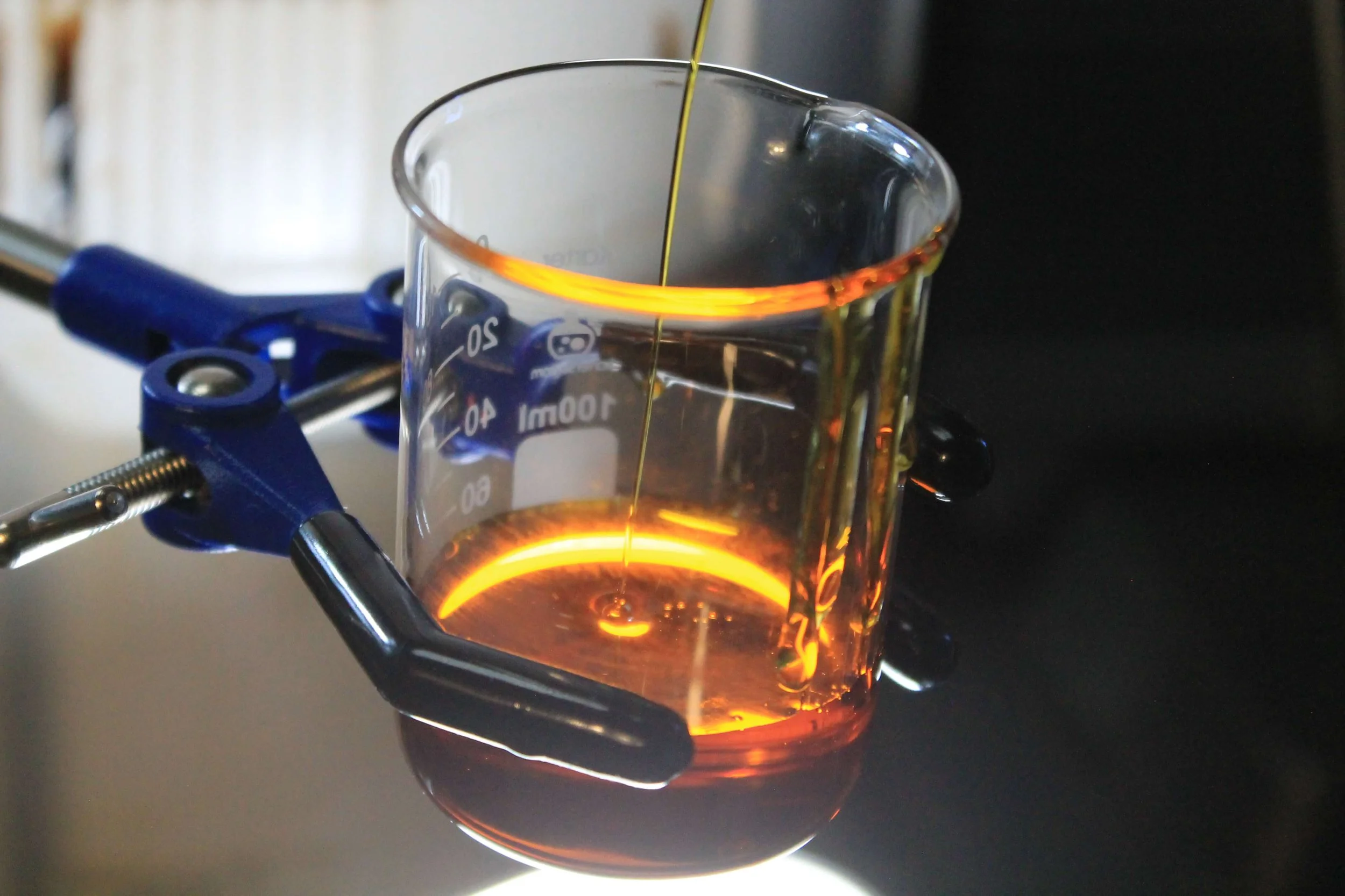 Laboratory beaker with amber concentrate extract being heated in clamp holder during purification process