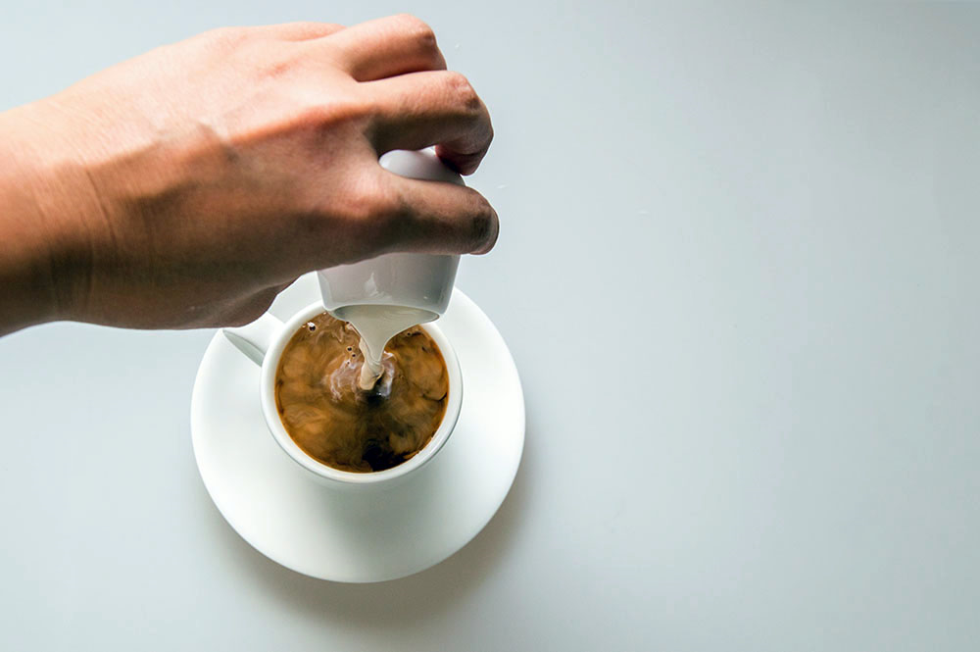 Person pouring creamer in coffee