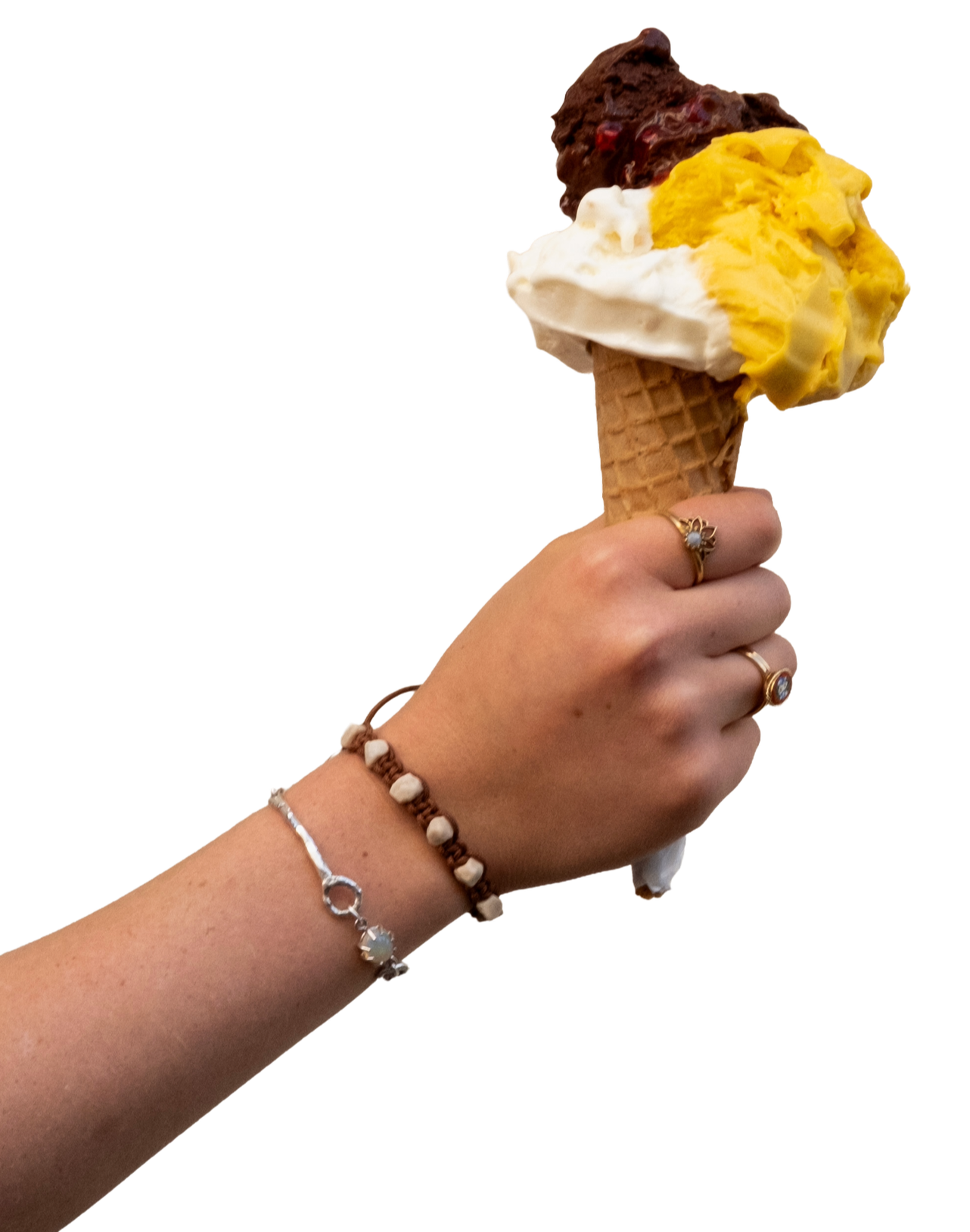 Hand holding an ice cream cone with three scoops of different flavored ice cream, including chocolate, vanilla, and mango, against a black background.