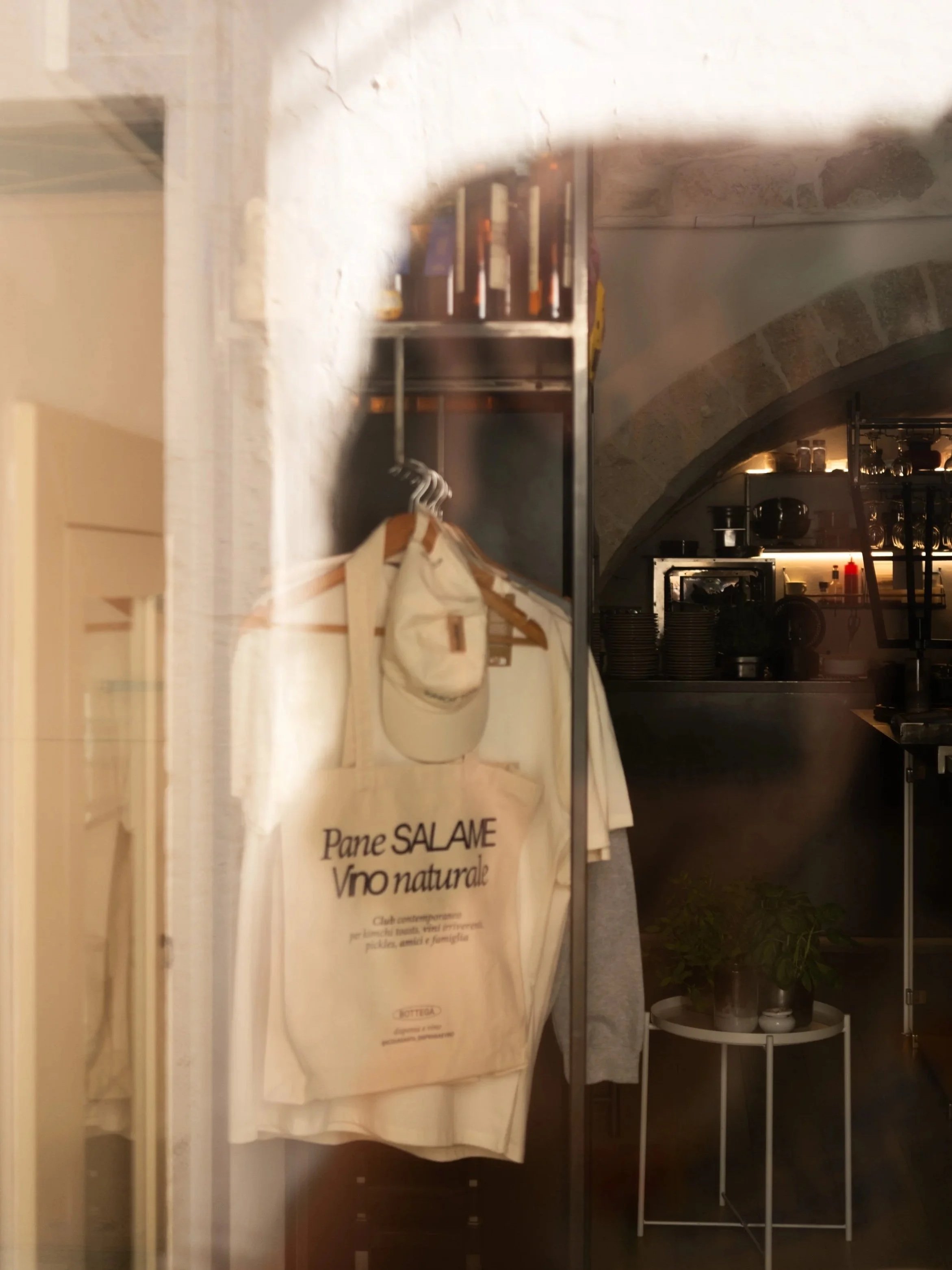 Photo looking through the window of a wine bar in Ostuni, Puglia showing tote bags, t-shirts, and merchandise available for purchase.