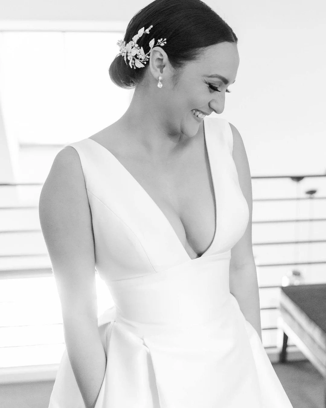 A woman in a wedding dress smiling and looking down, with her hair styled in an updo and decorated with a floral hairpiece.