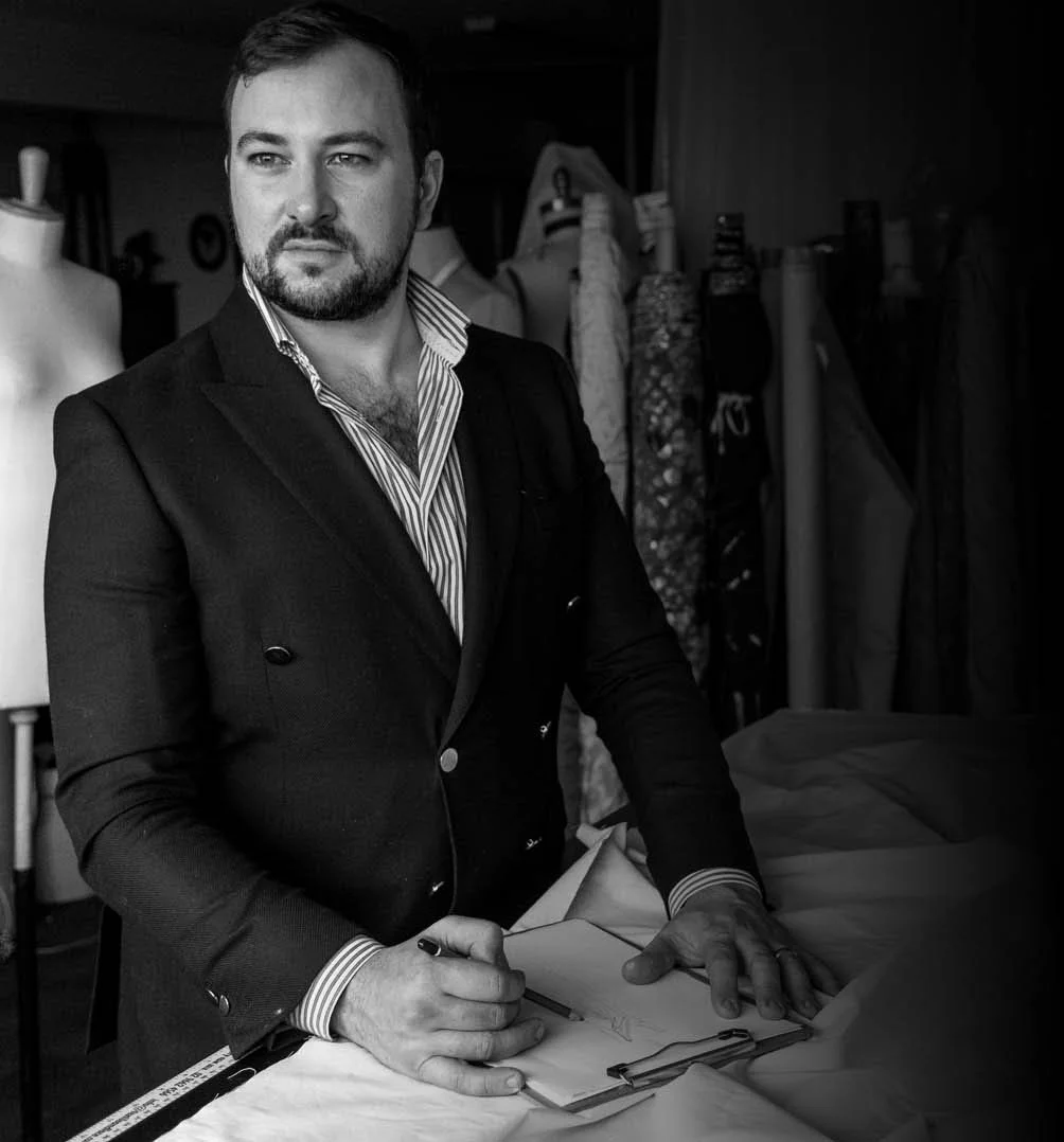 A man in a suit signing fabric on a table in what appears to be a sewing or fashion studio.