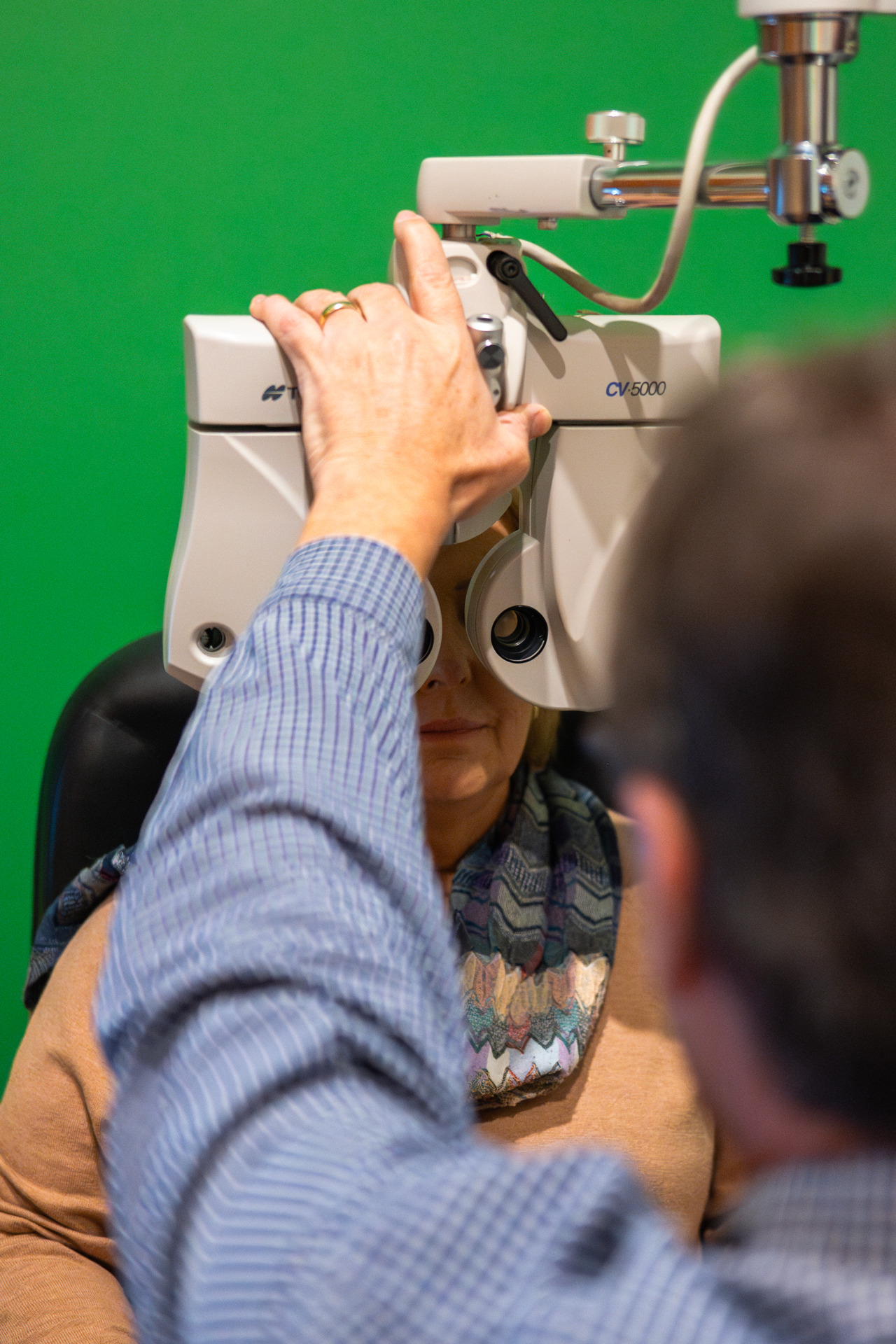 A woman undergoes an eye examination using a slit lamp machine, with a green background.