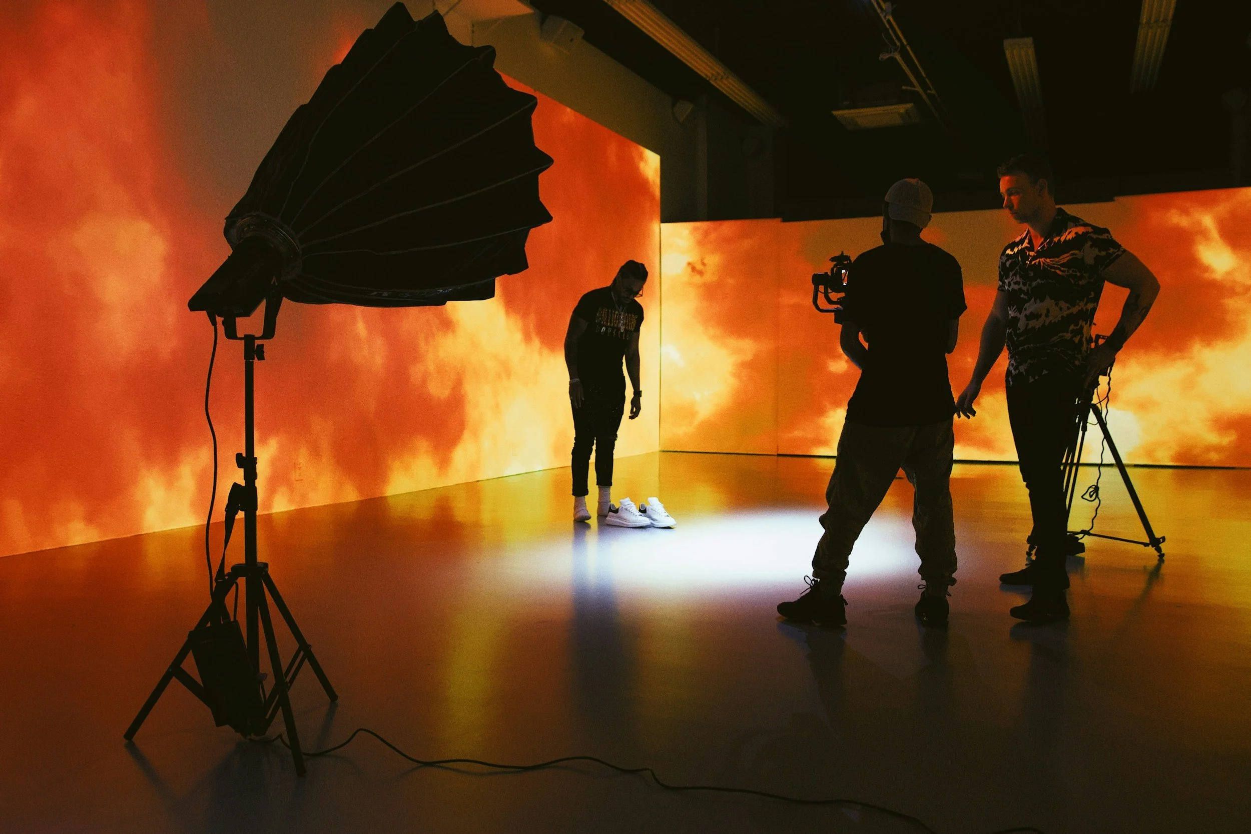 People filming a woman in a studio with an orange and yellow fiery background, large studio light on lamp stand, and camera operators.