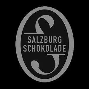 Logo with a black background and gray oval, containing a stylized 'S' and the words 'Salzburg Schokolade'.