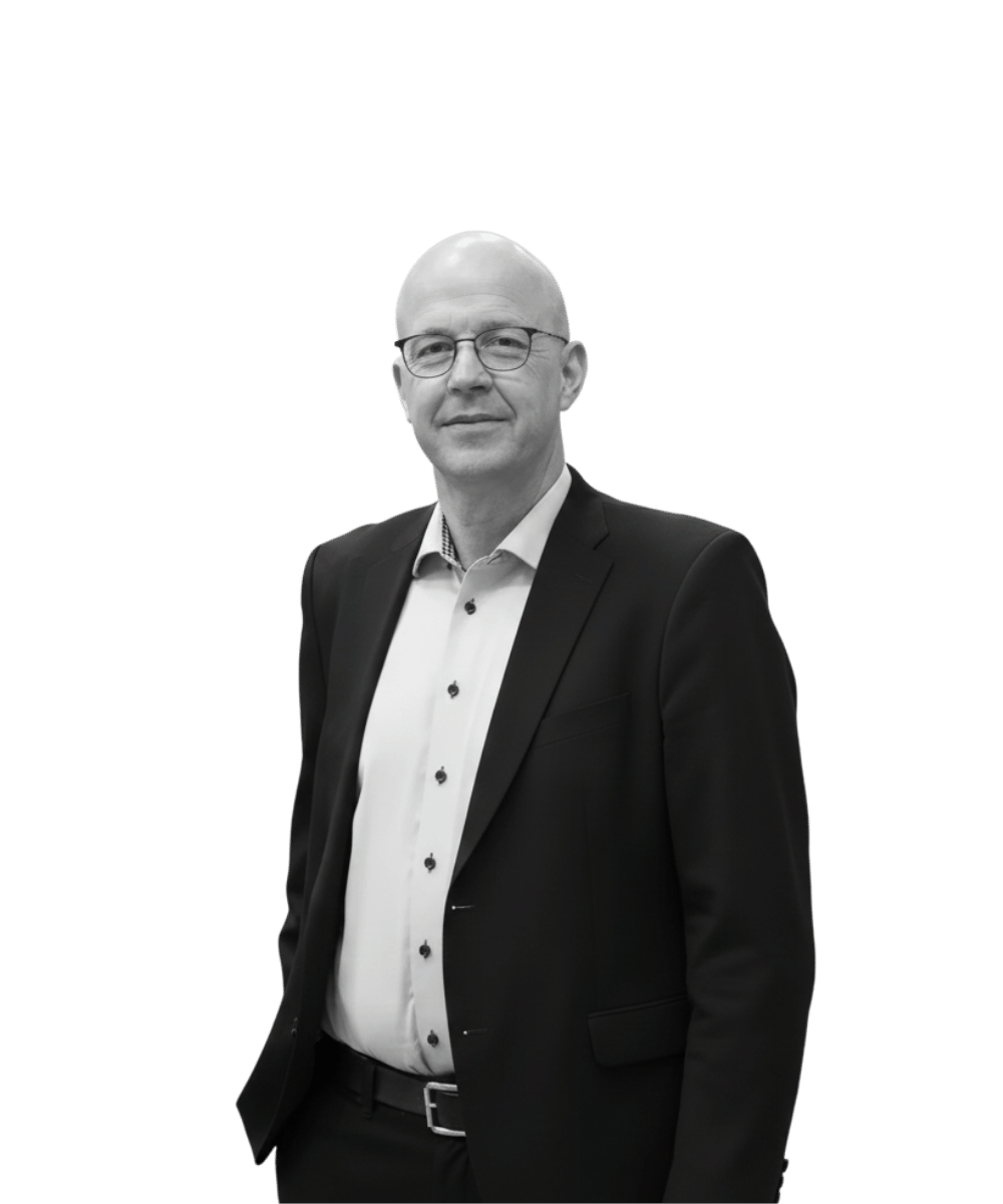 A middle-aged man with glasses, wearing a black suit and white shirt, standing against a black background.