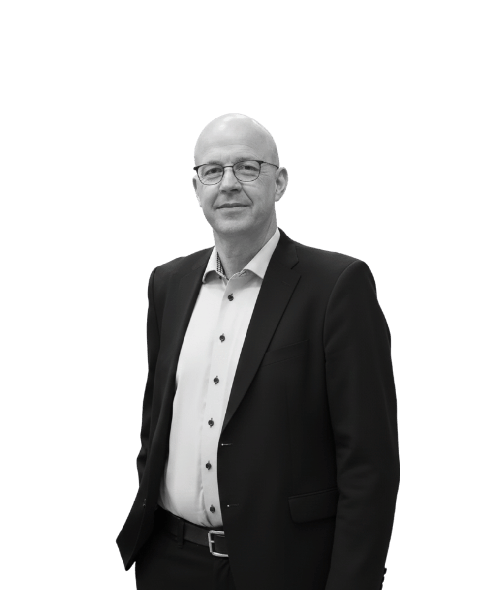 A middle-aged man with glasses, wearing a suit jacket and a button-up shirt, standing against a black background.