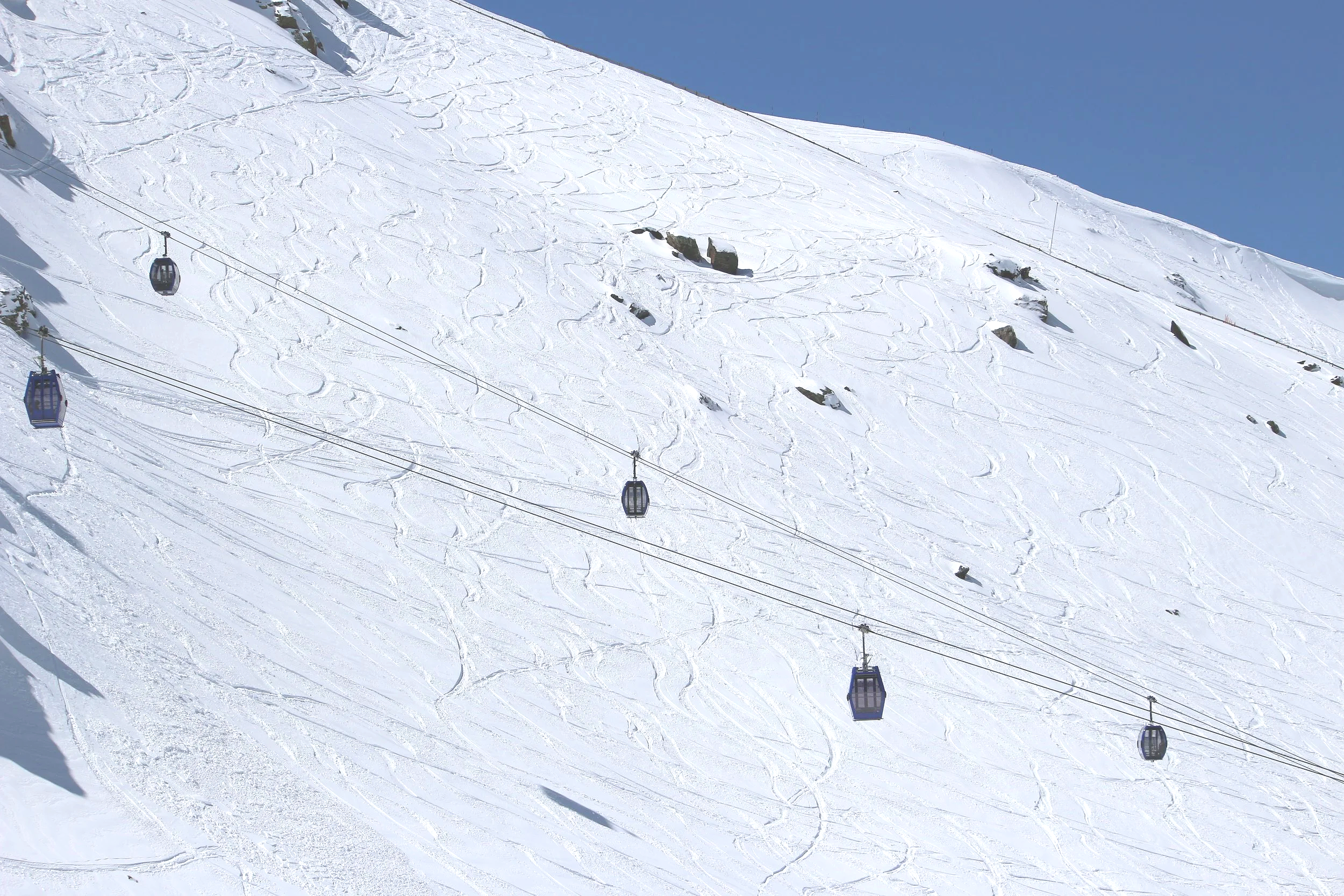 Snow-covered sierra nevada and a cable car line with several cabins on a clear, sunny day.