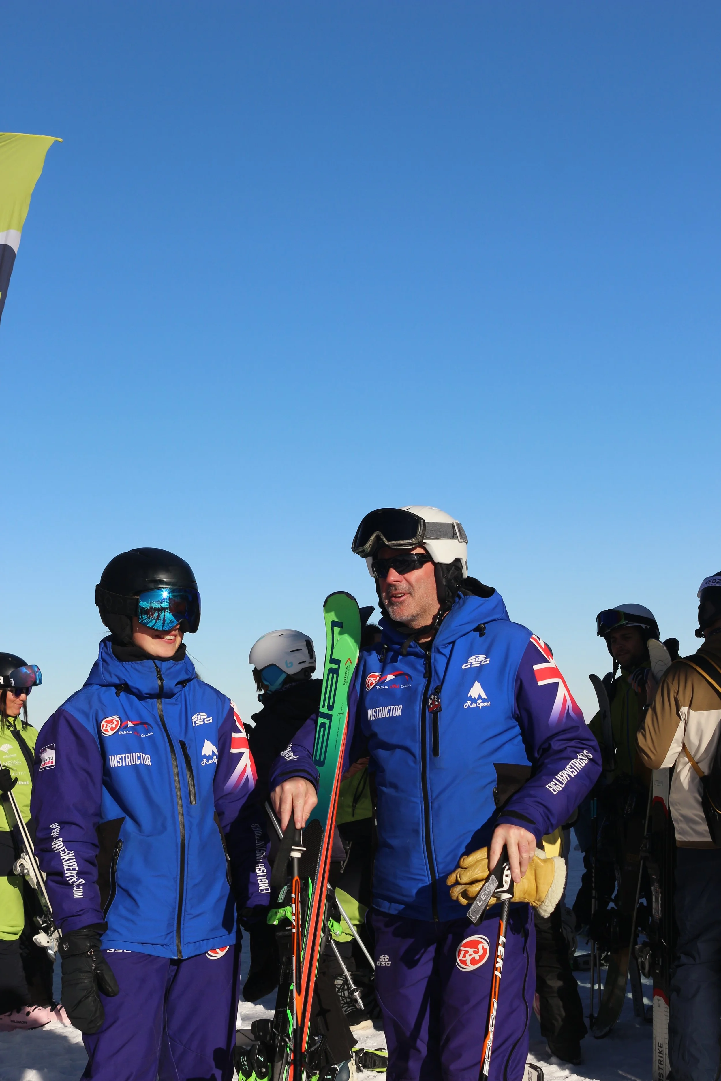Group of ski instructors on a snowy mountain, wearing blue jackets, helmets, and goggles.