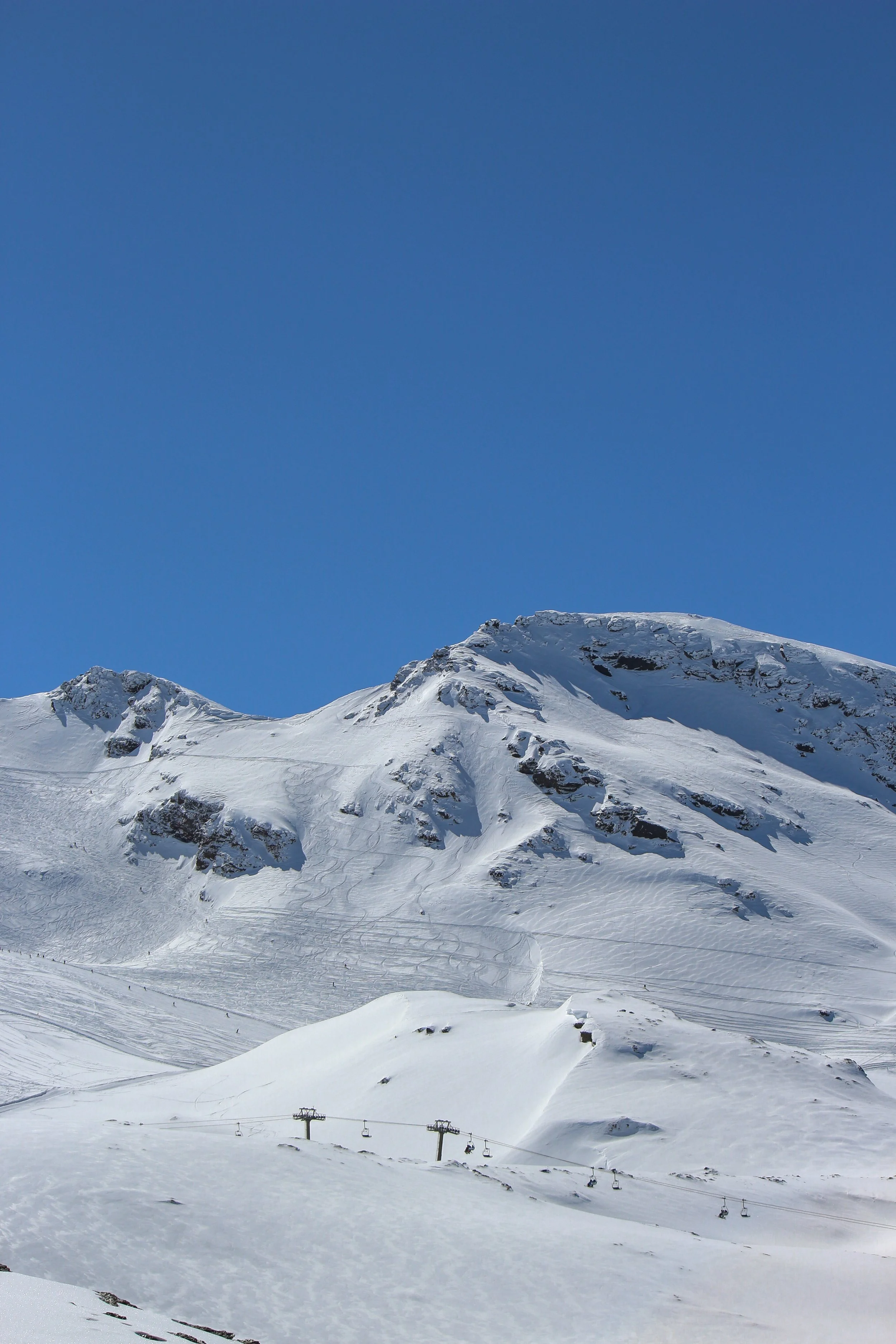 Snow-covered mountain in Sierra Nevada with ski lift and skis in the snow, clear blue sky.