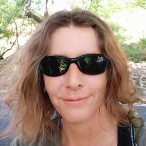 Woman with wavy hair wearing sunglasses outdoors in a natural setting