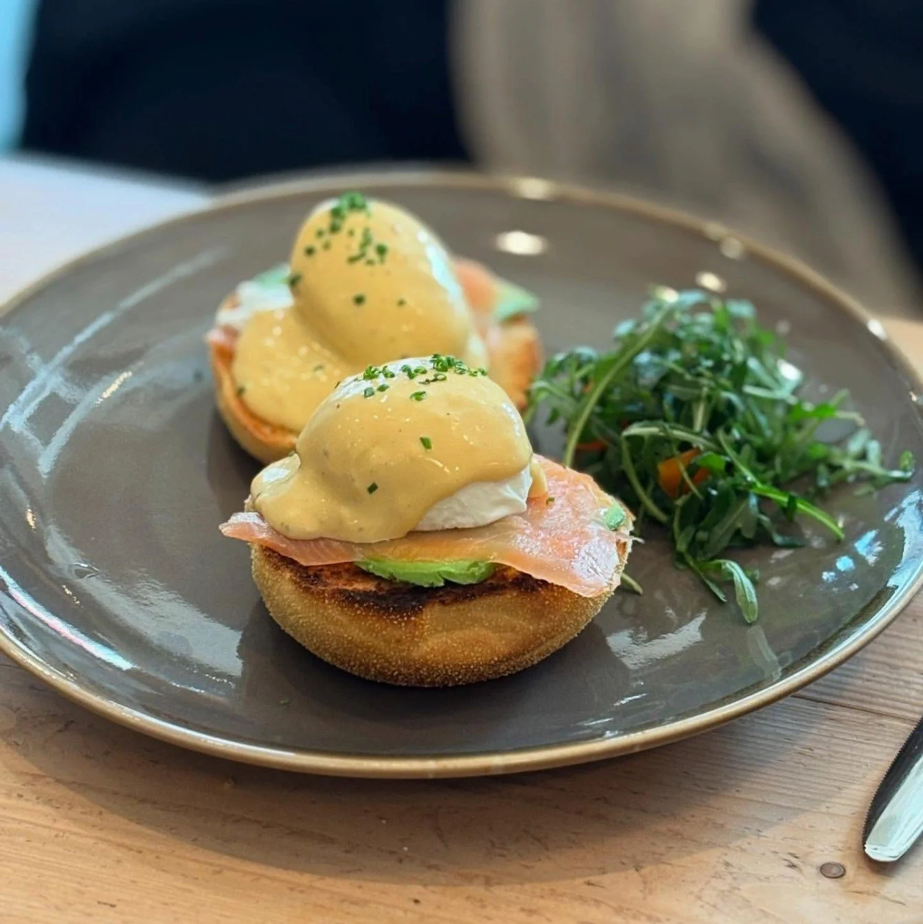 Plate of eggs Benedict with smoked salmon, topped with hollandaise sauce, served with a side of arugula salad.