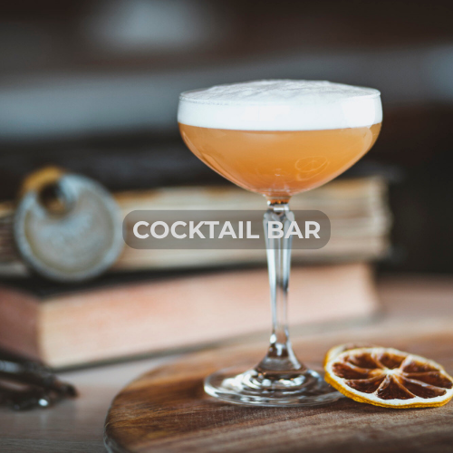 A cocktail in a coupe glass with a foamy top, placed on a wooden surface with a dried lemon slice nearby, and the words 'COCKTAIL BAR' overlayed.