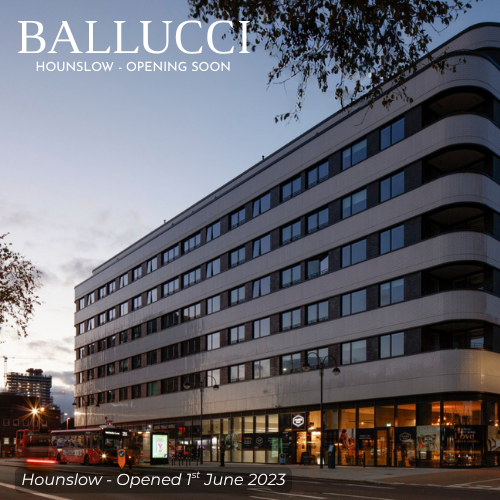 Photo of a modern multi-story building with curved architecture, large windows, and retail shops on the ground floor, under a partly cloudy sky during dusk.