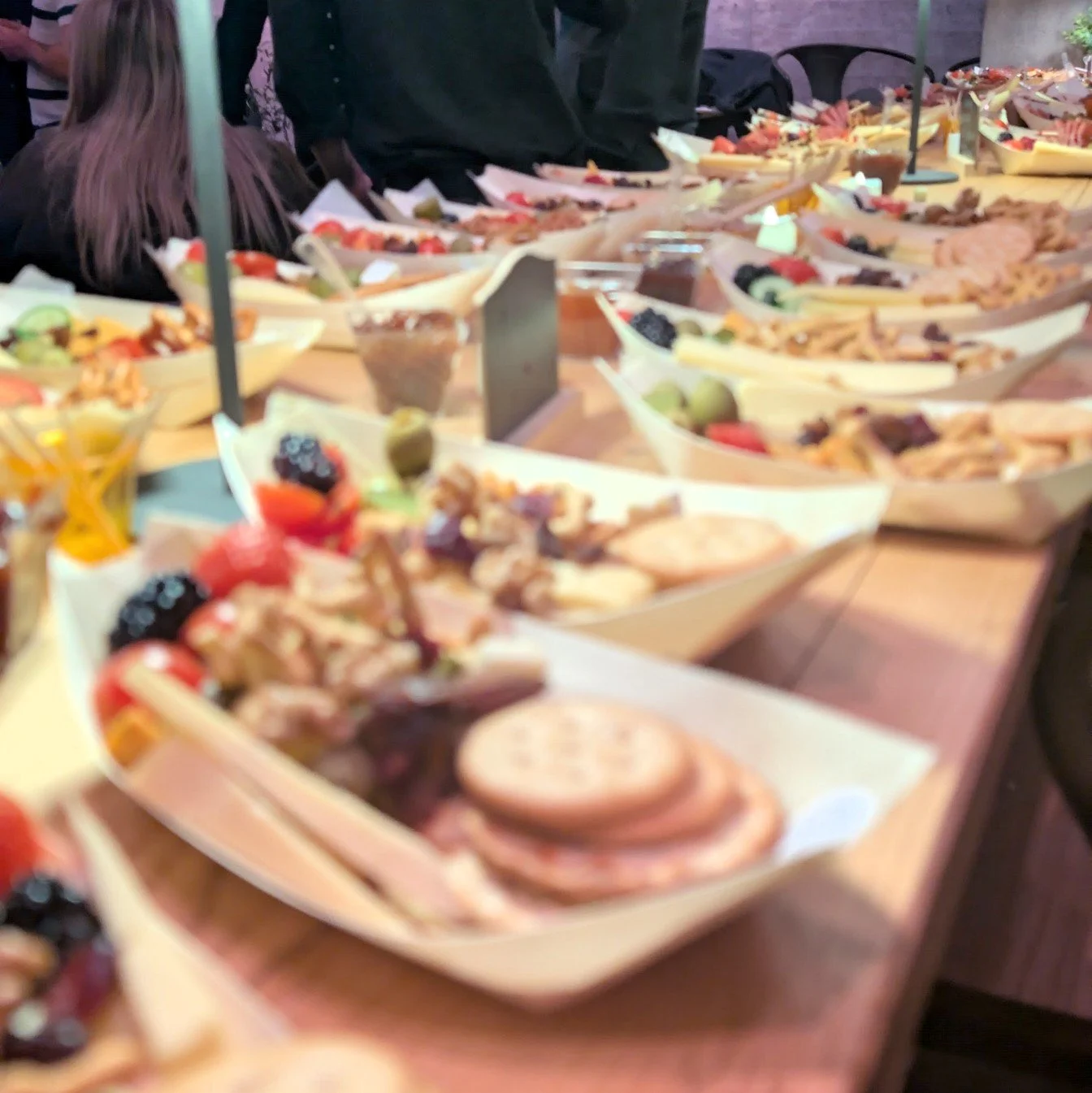 A table filled with small boats of food, including fruit, cookies, and salads, at a social event.