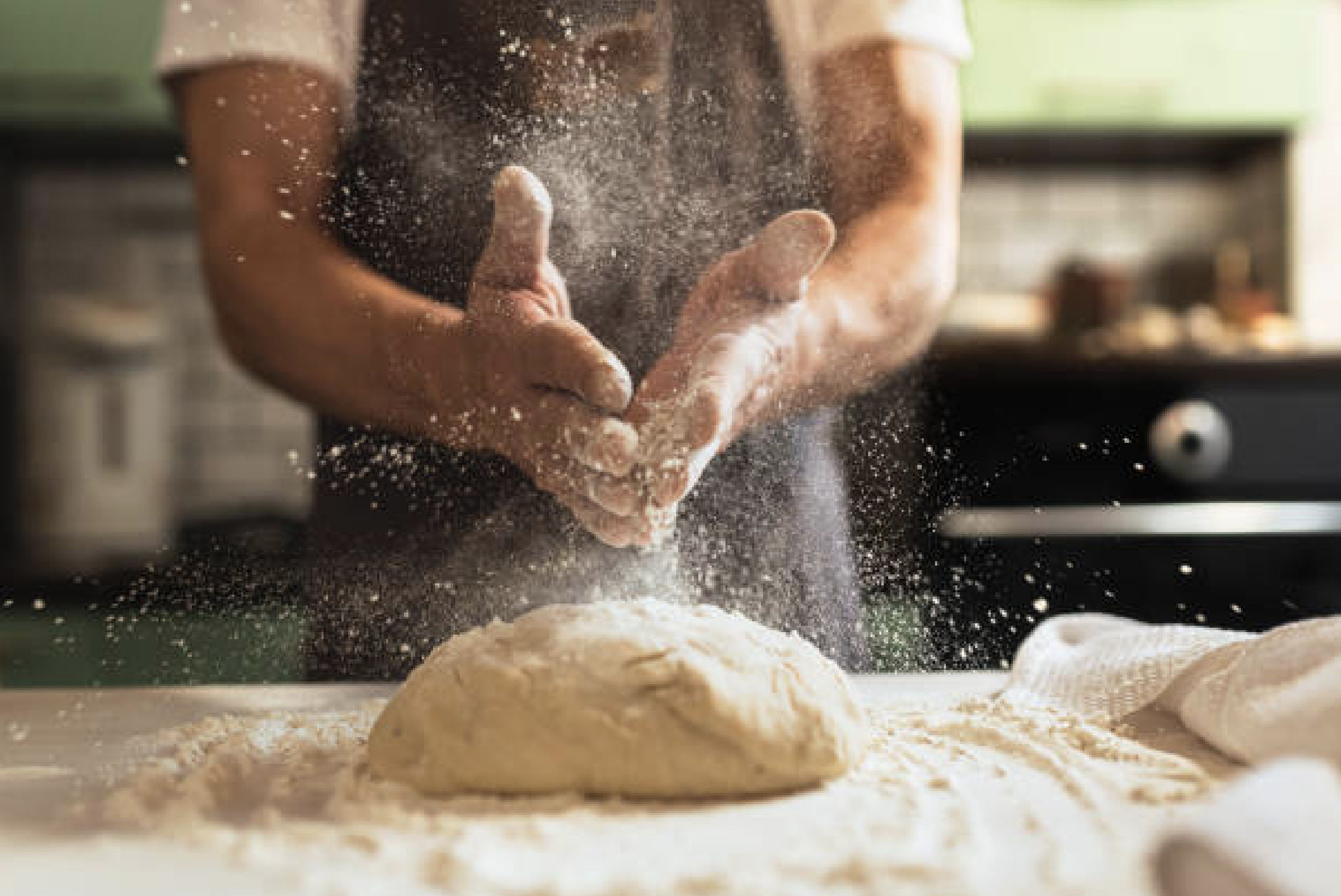 Close-up of a person sprinkling flour onto dough during baking in a kitchen.