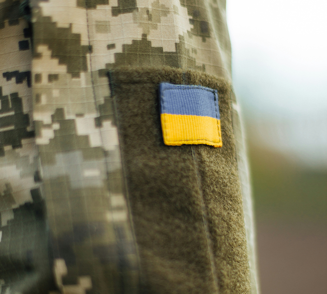 Close-up of a military uniform sleeve with a camouflage pattern and a Velcro patch featuring the Ukrainian flag.