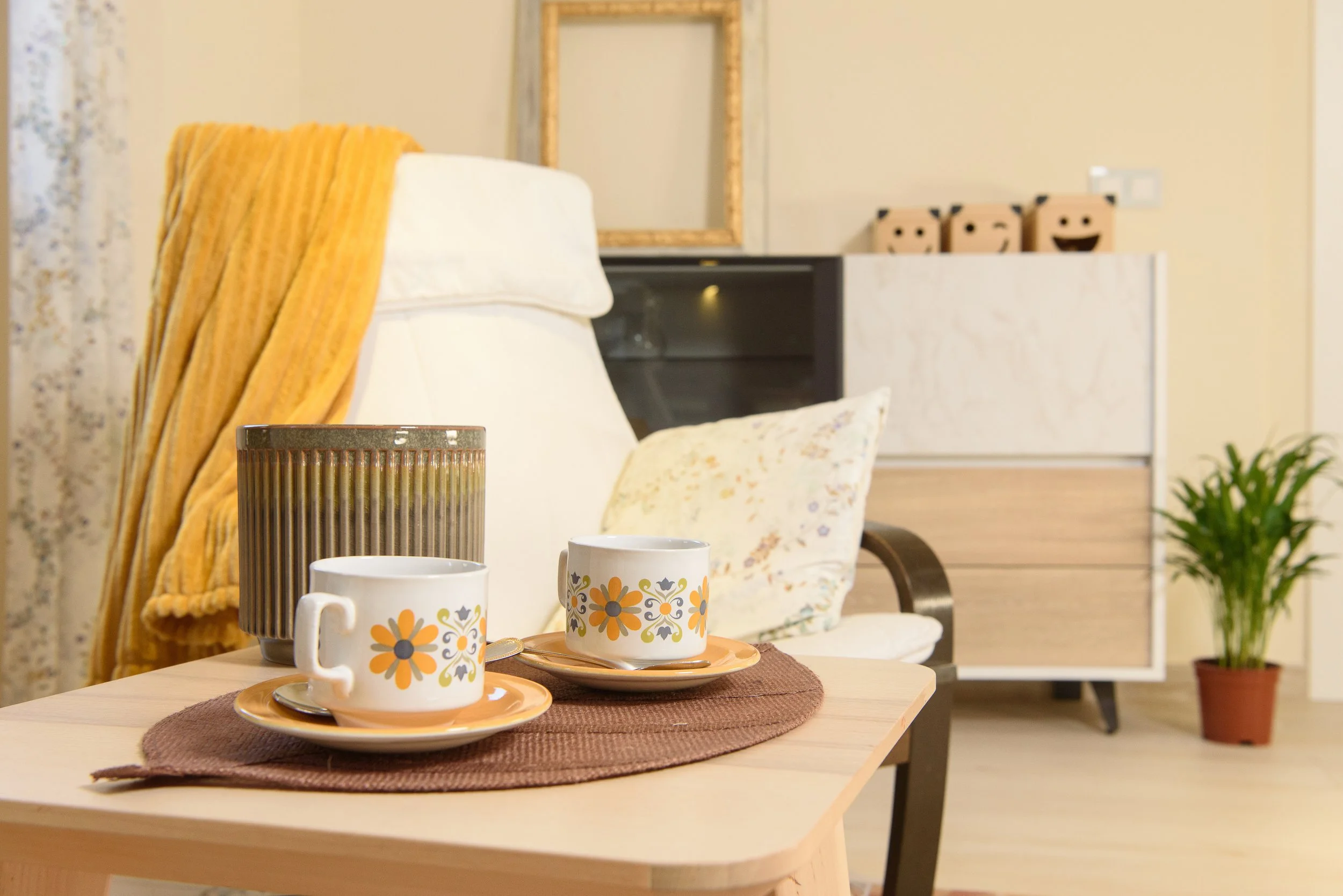 Mesa con dos tazas y platos en una sala decorada con cojines, planta y armario