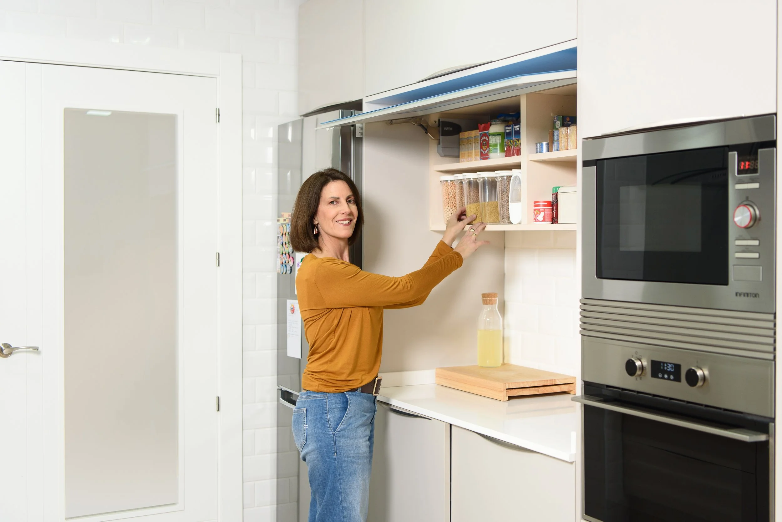 Mujer organizando especias en una despensa de cocina moderna con electrodomésticos de acero inoxidable.