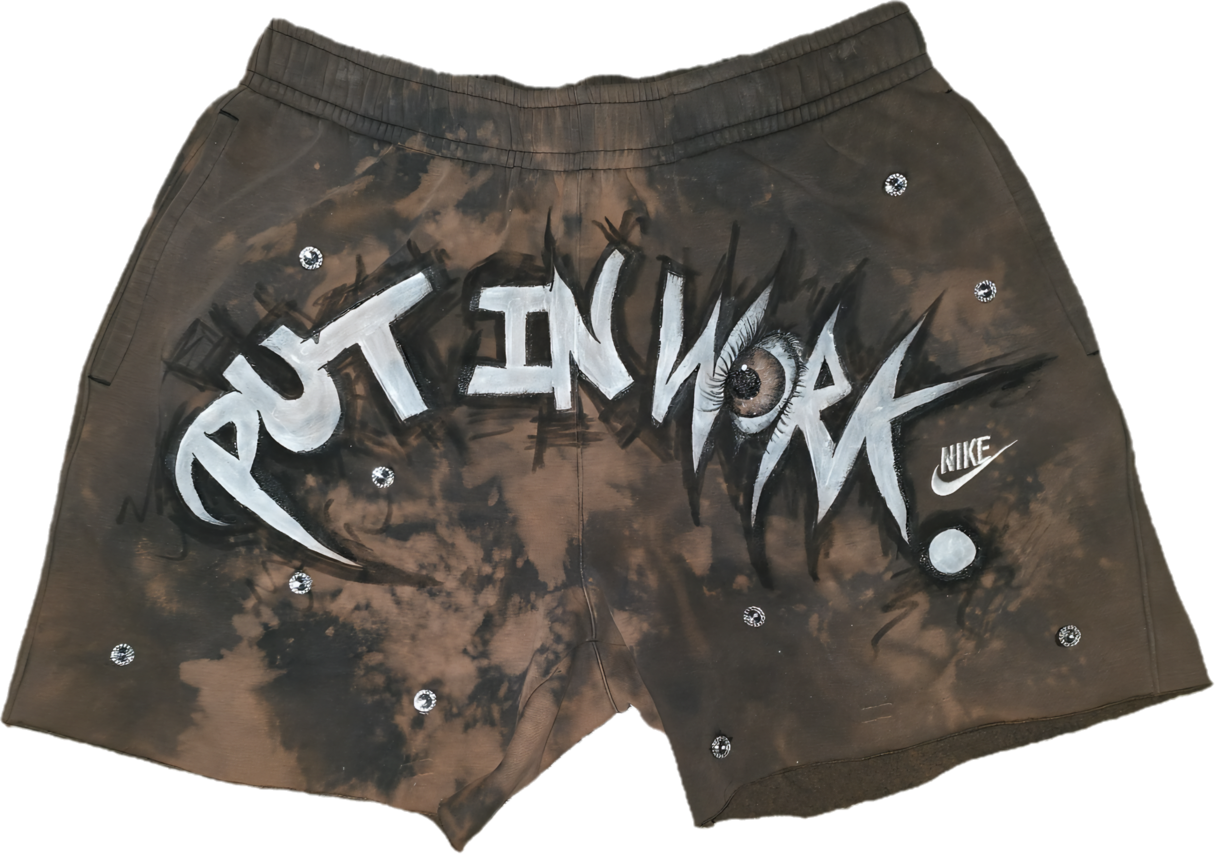 Brown shorts with white painted and black spray-painted graffiti style text that reads "PUT IN WORK" along with sparkly rhinestone embellishments, a painted eye illustration, and a Nike logo.