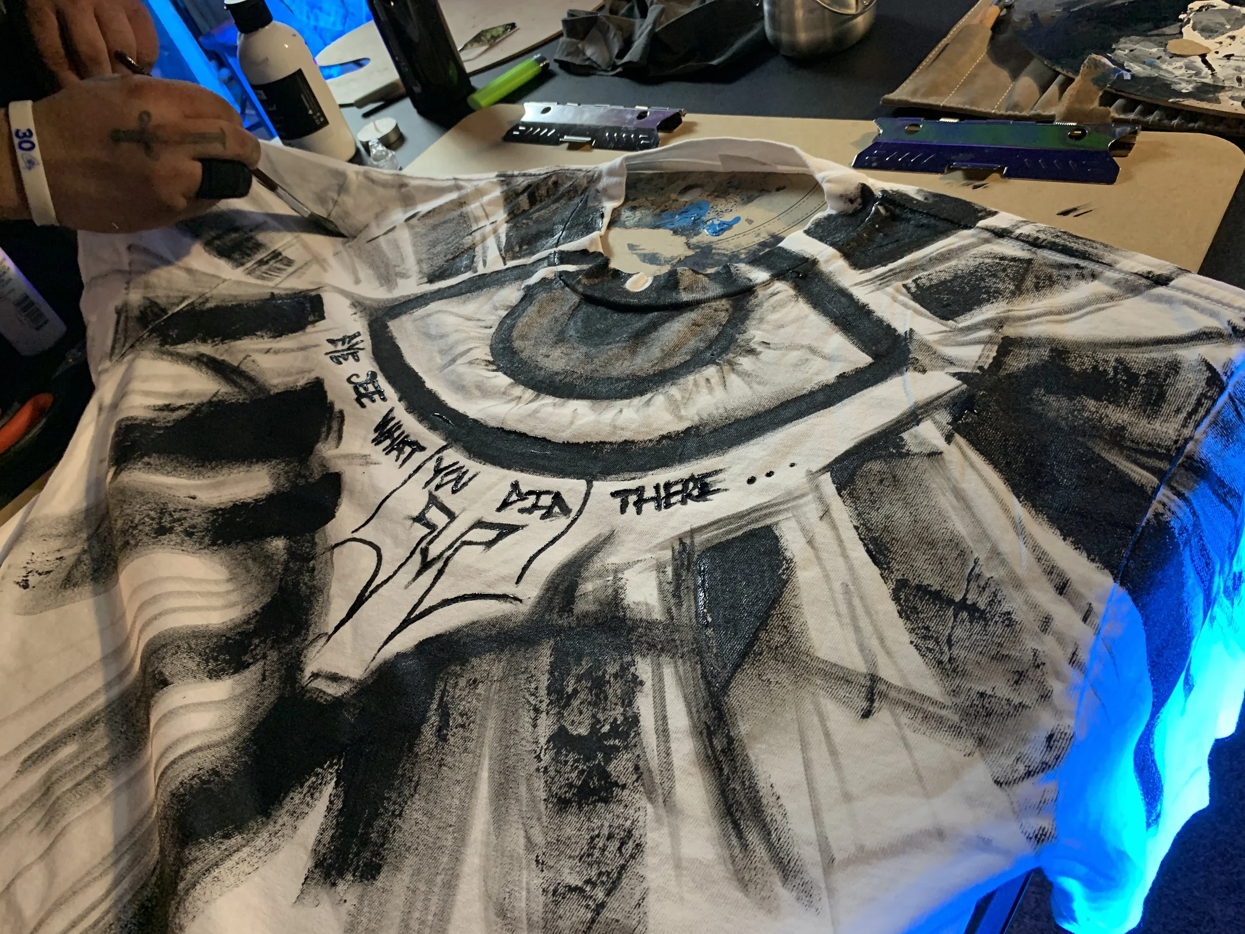 Hand painting abstract design on a white T-shirt with text saying "We see what you did there..."