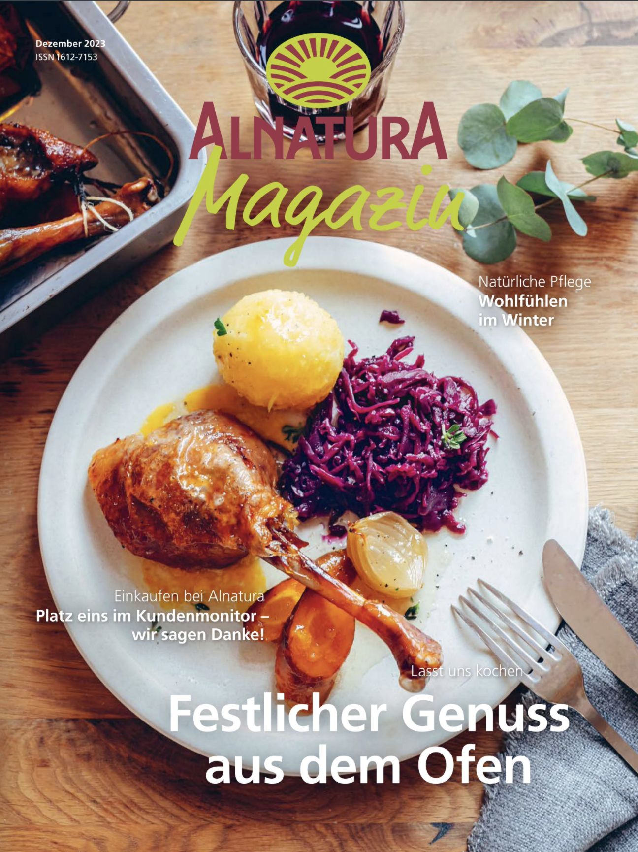 A magazine cover featuring a plate of cooked meat with vegetables and purple cabbage, a glass of red wine, and a side dish of roasted vegetables on a wooden table, with a fork and knife on a gray napkin. The magazine is titled 'Alnatura Magazin' and includes headlines about winter care and cooking.