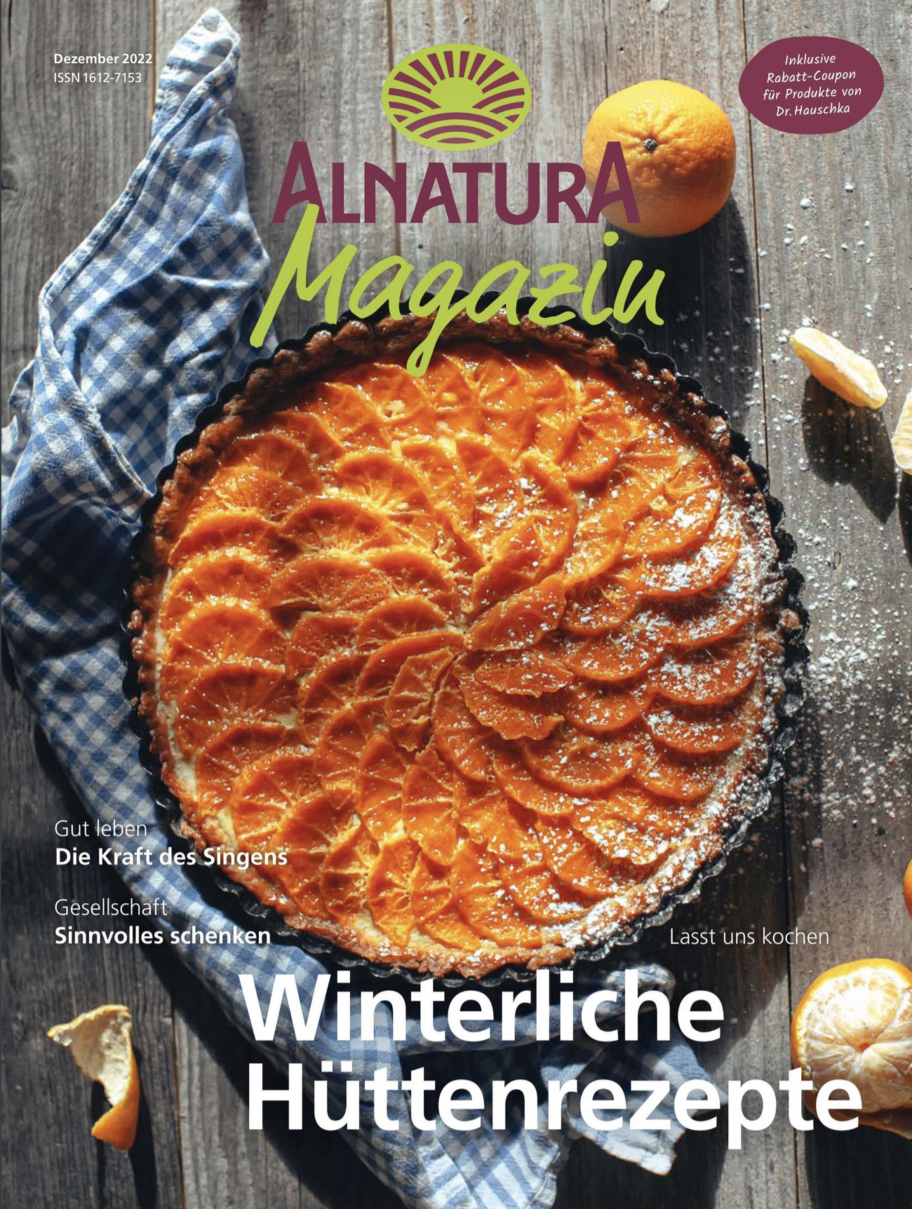 A magazine cover featuring a citrus tart topped with sliced oranges, placed on a rustic wooden surface with scattered lemon and orange slices and a blue checkered cloth.