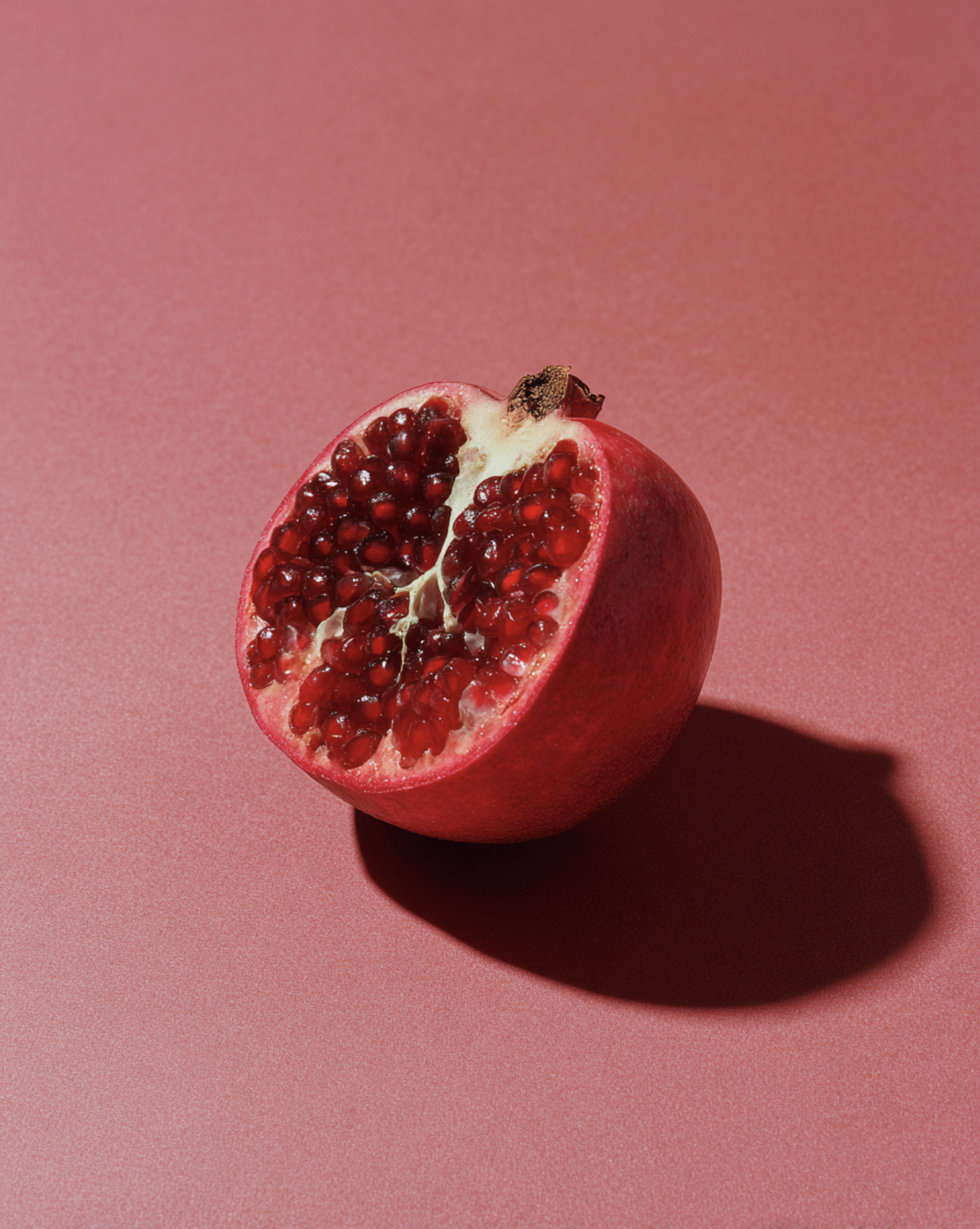 A halved pomegranate on a pink surface with a shadow cast to the right.