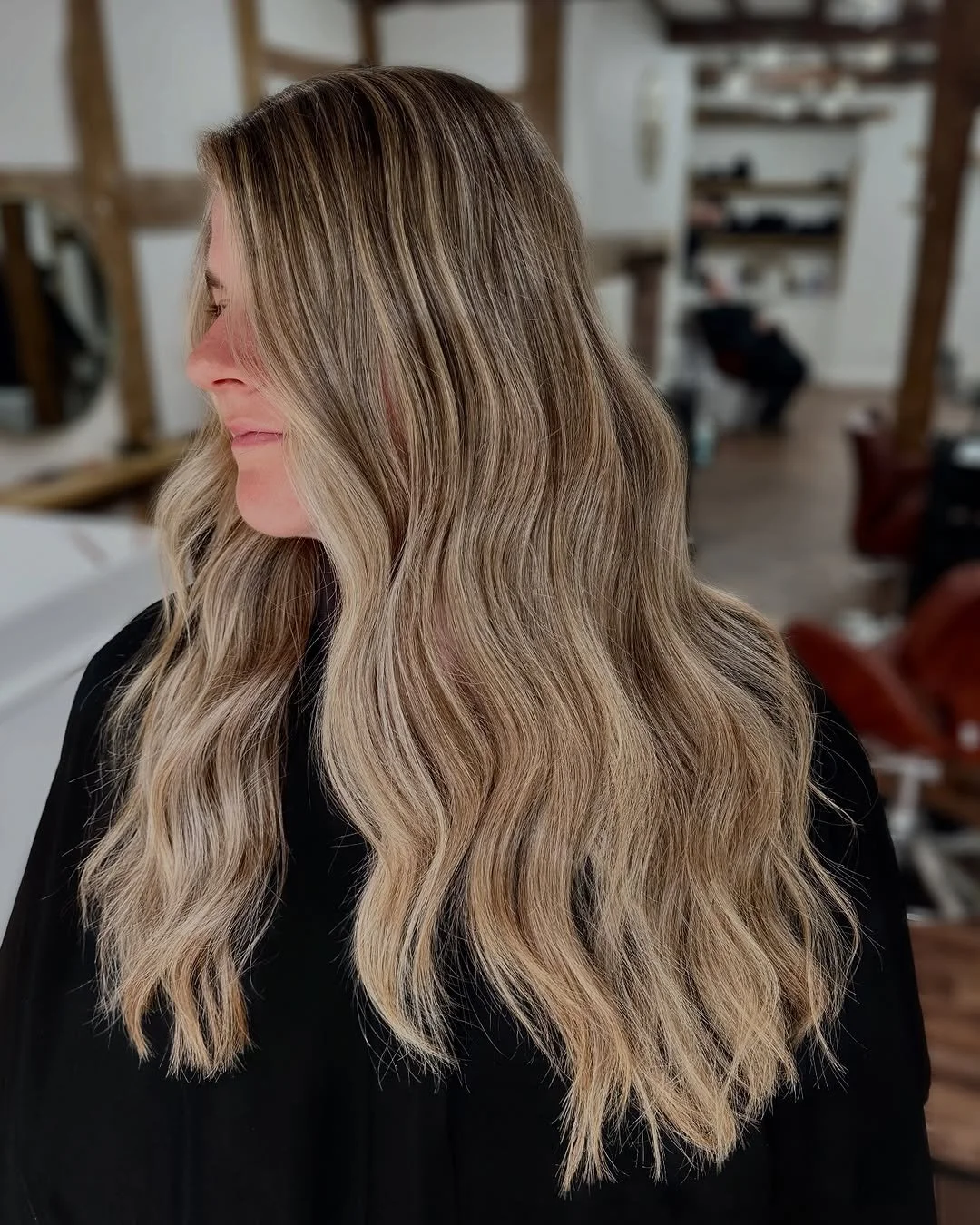 A woman with long, wavy blonde hair looking to her left in a salon or beauty studio.